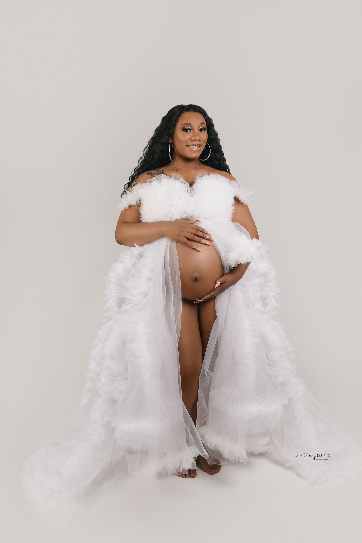 A maternity photo featuring a woman wrapped in white tulle against a light background.