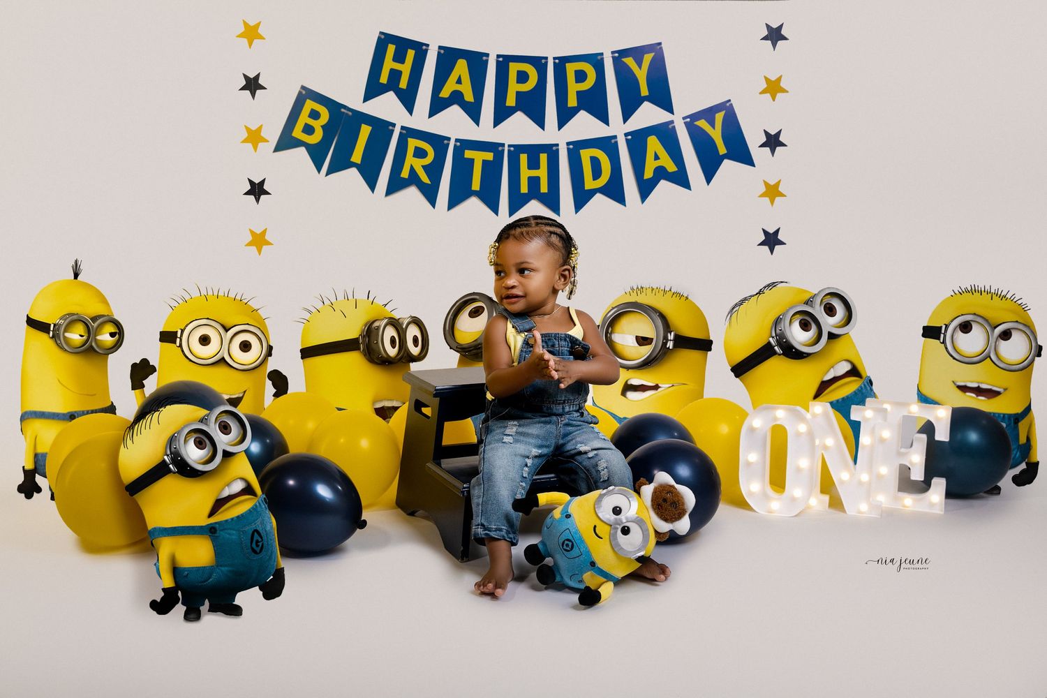 Child sitting with Minion characters at birthday party celebration with blue banner.