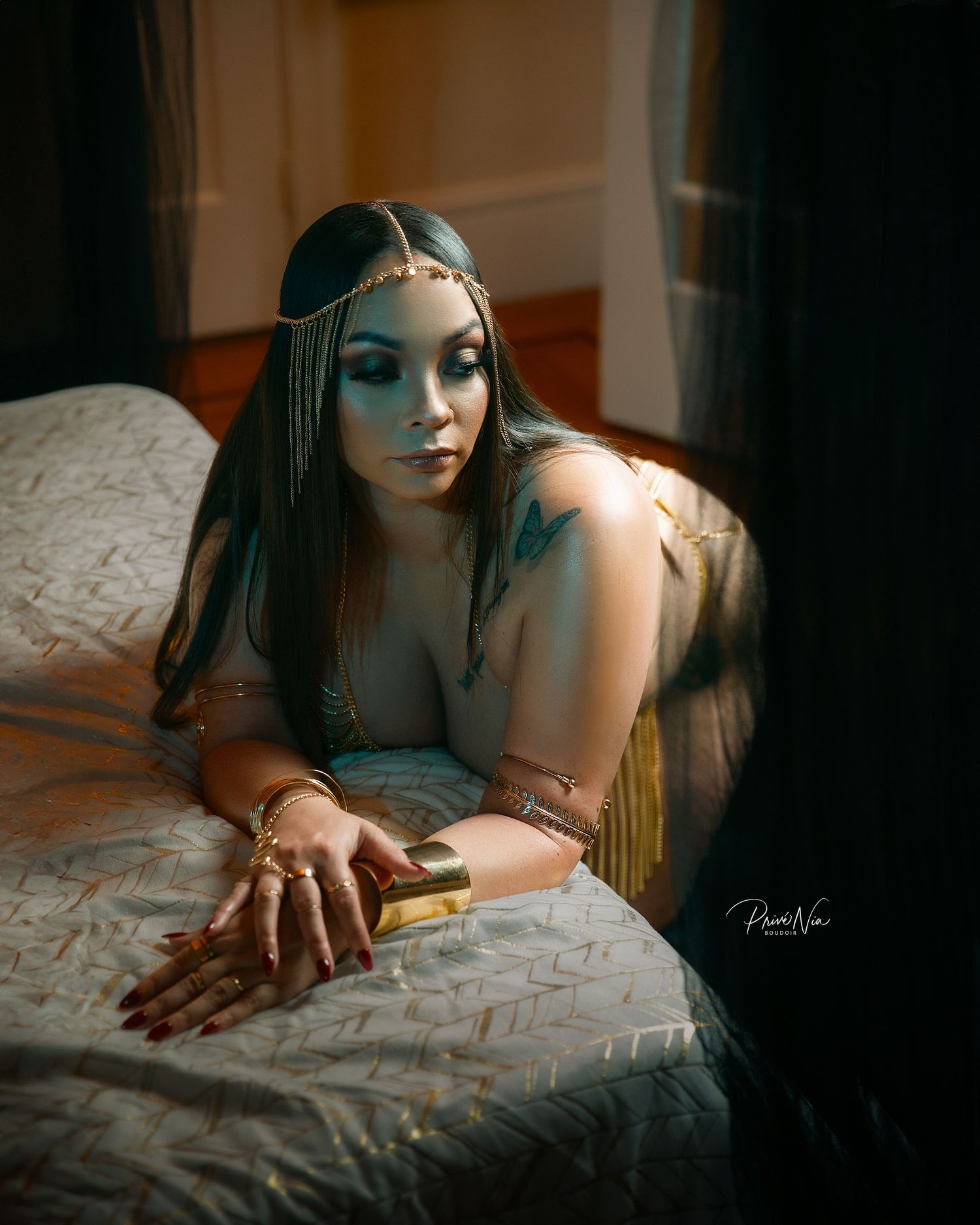 Glamorous boudoir portrait with dramatic lighting and ornate metallic headpiece.