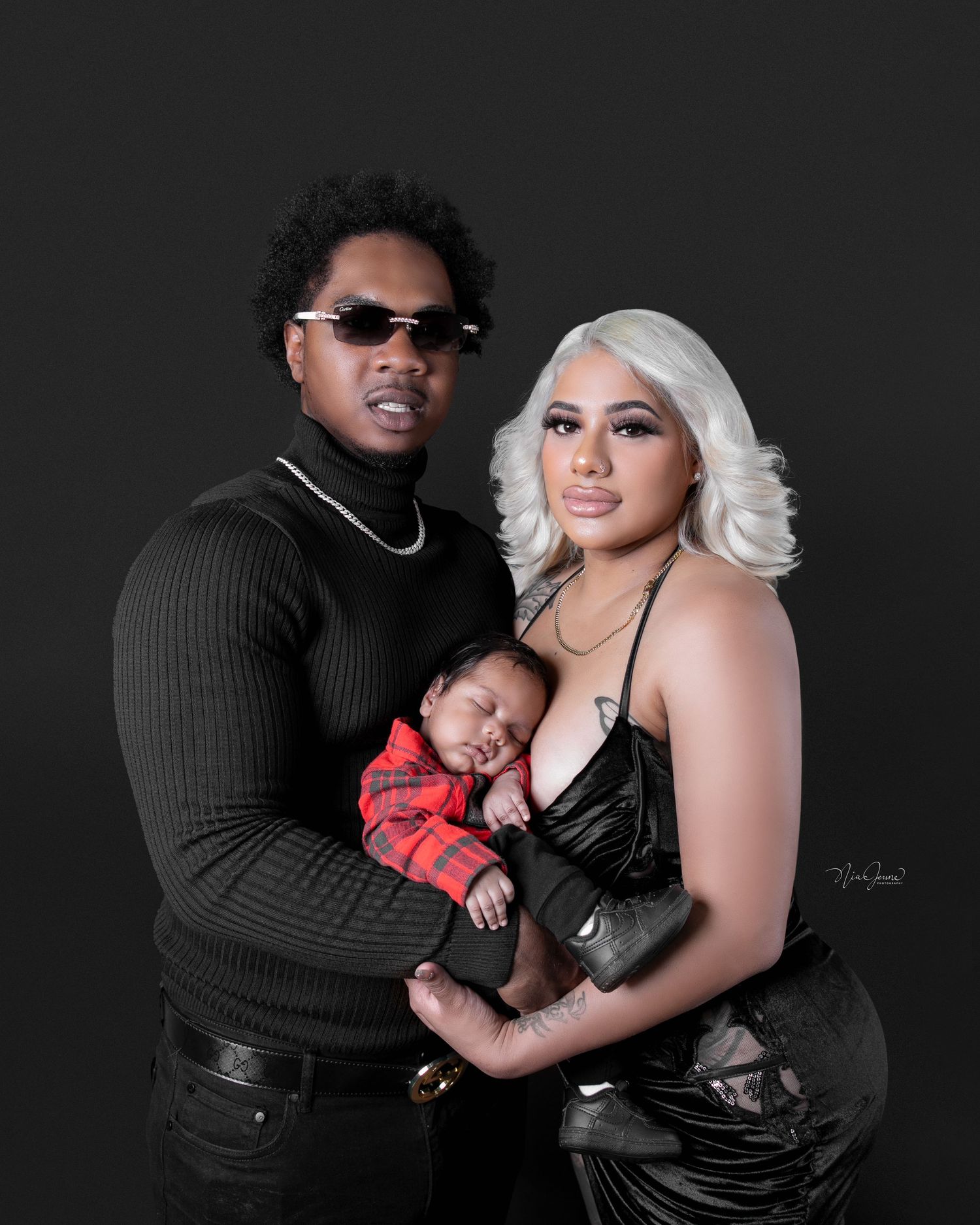 Family portrait with infant in dark attire against black background.
