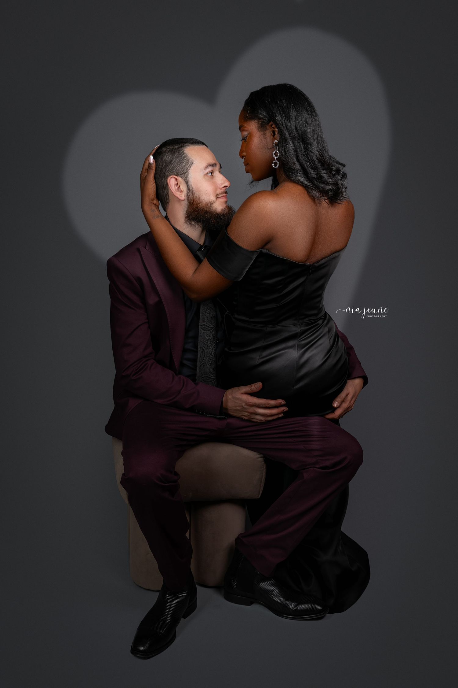 Romantic couple portrait with dramatic lighting showing intimate embrace against dark background.
