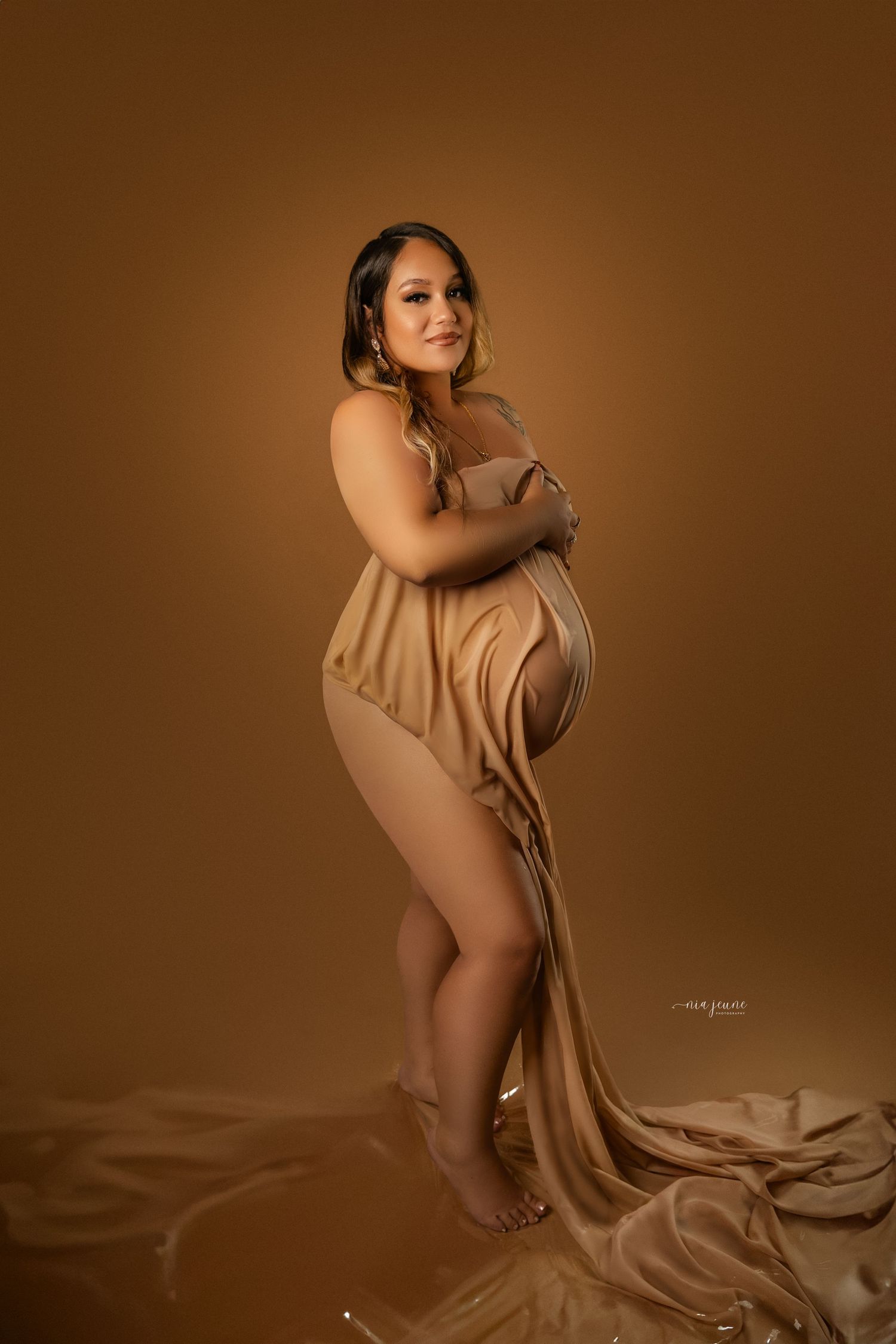 Artistic maternity photography with flowing fabric against warm brown background.