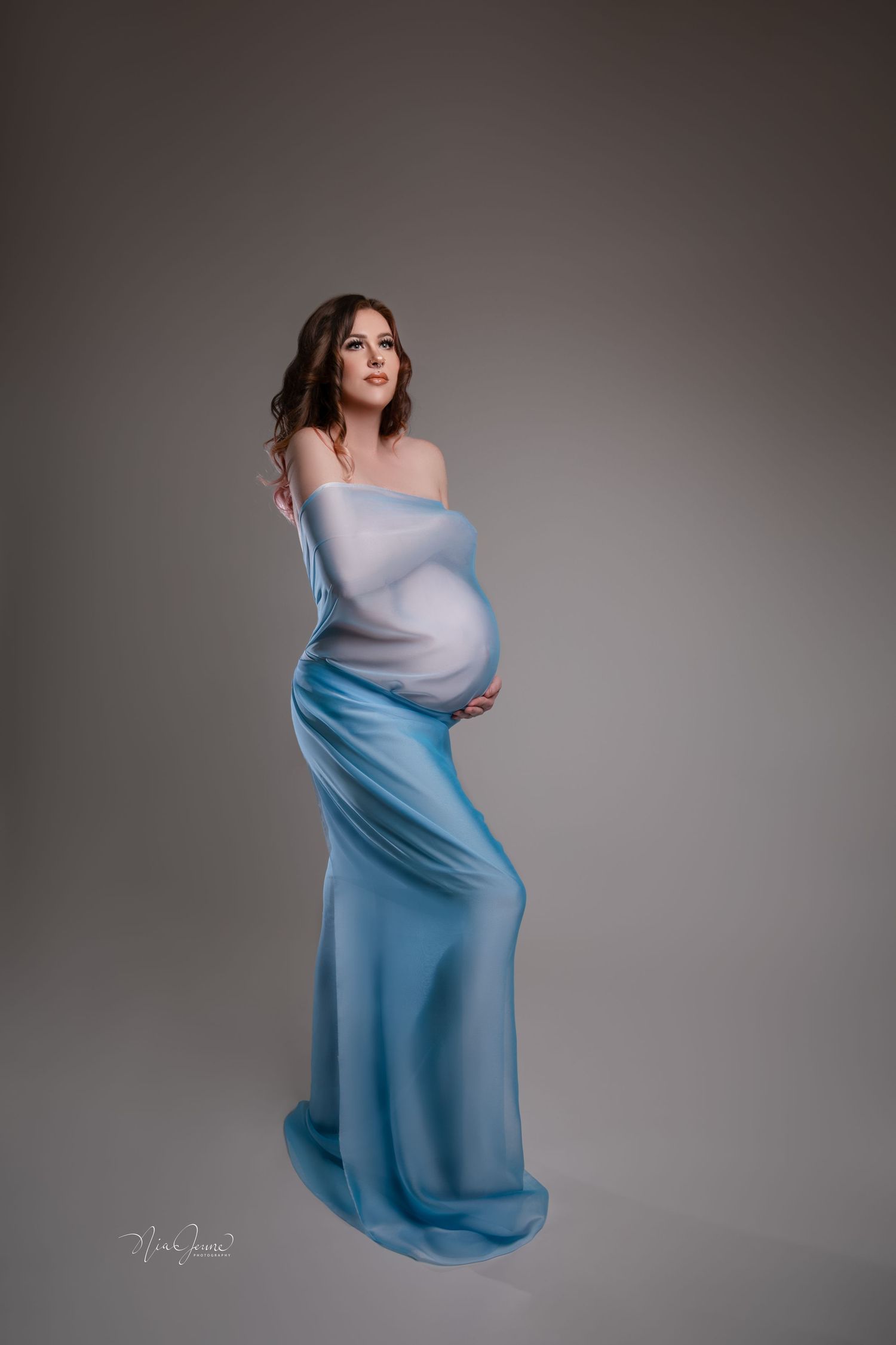 Maternity portrait in flowing blue dress against dark background.