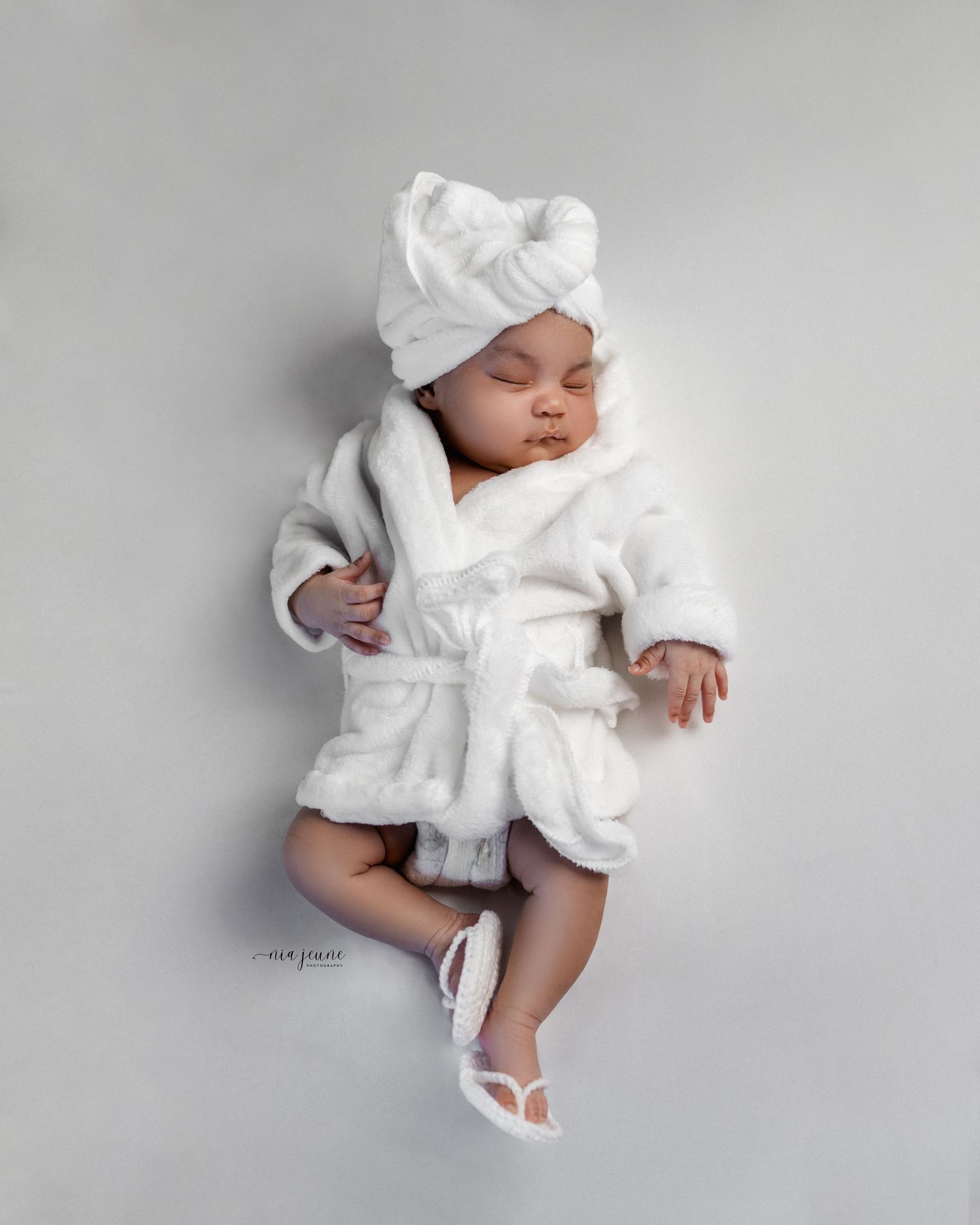 Series of photos showing an infant in white clothing and bonnet laying on grey background.