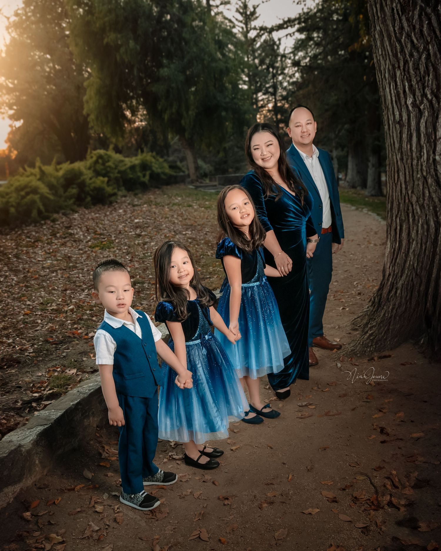 Family photo session on woodland path with children in coordinating blue outfits.