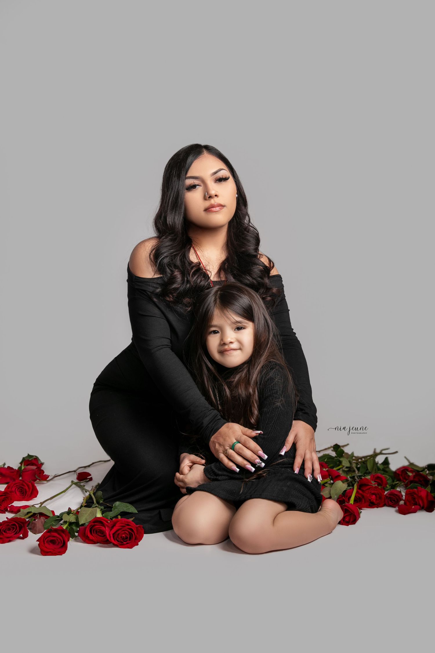 Artistic boudoir photoshoot featuring red roses and black clothing against a grey backdrop.
