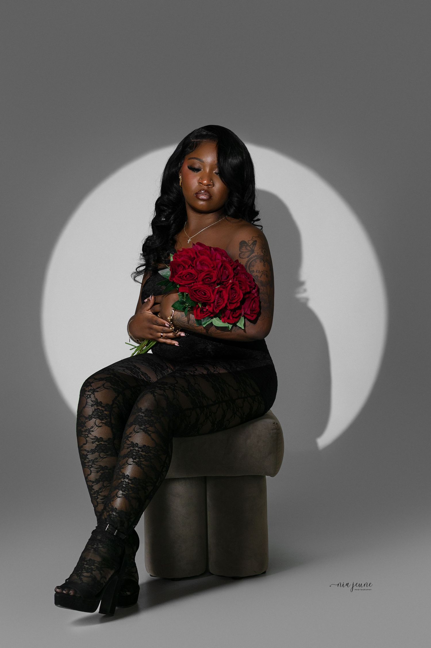 Elegant studio portrait with red roses against a dramatic circular backlight on a gray background.
