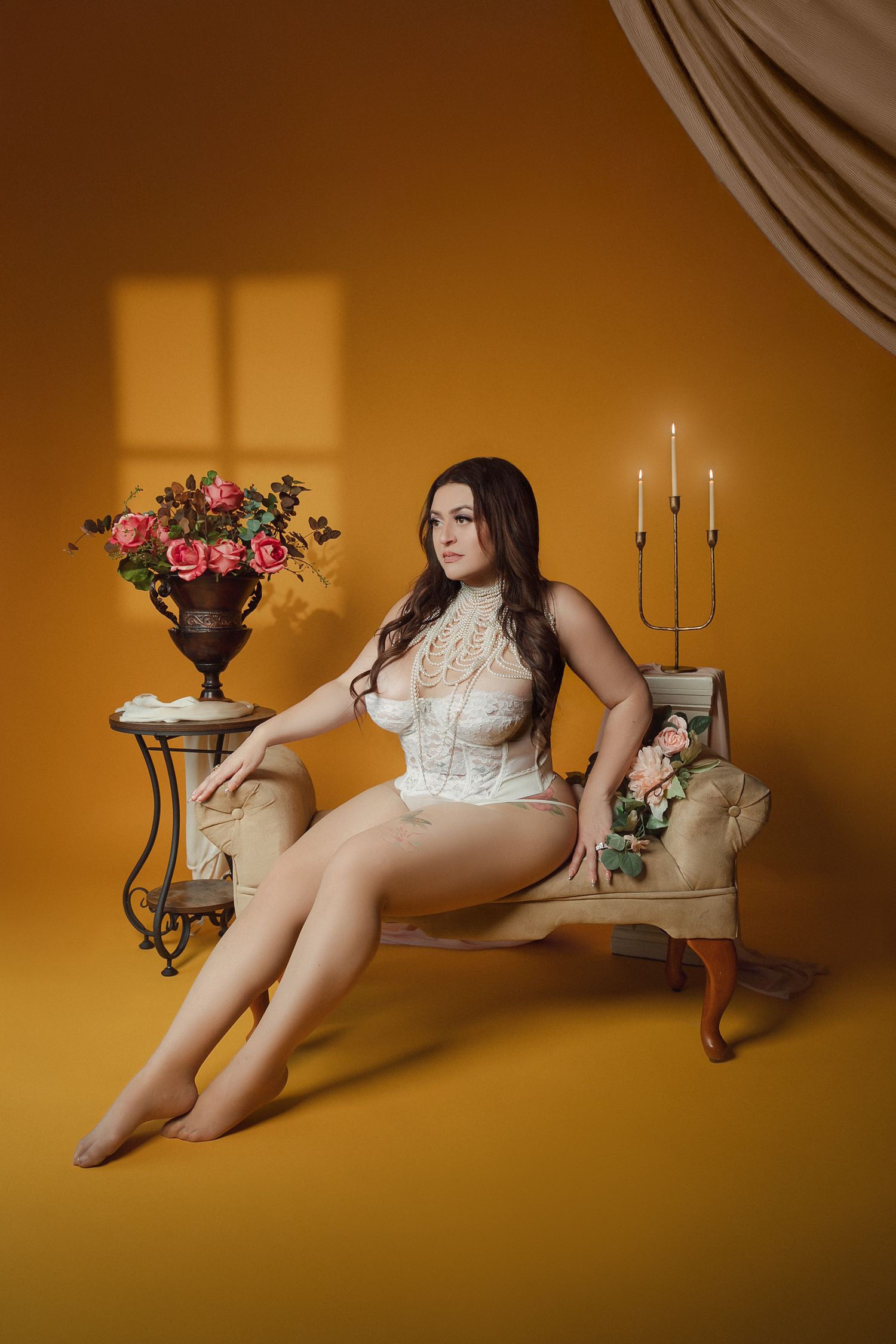 Elegant boudoir portrait in white lingerie against golden walls with antique furniture and flowers.
