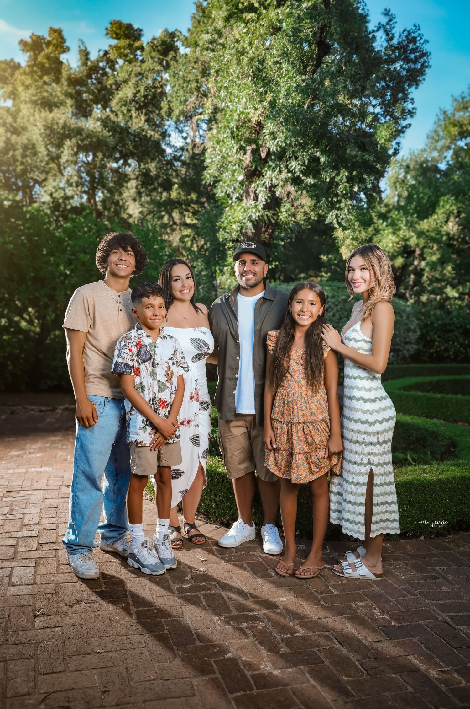 Family photo session outdoors with multiple poses on brick steps surrounded by green trees.