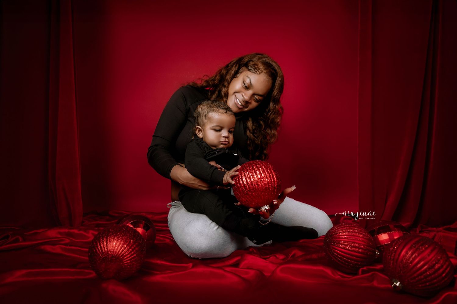 Professional Christmas photo session with red backdrop and holiday decorations.