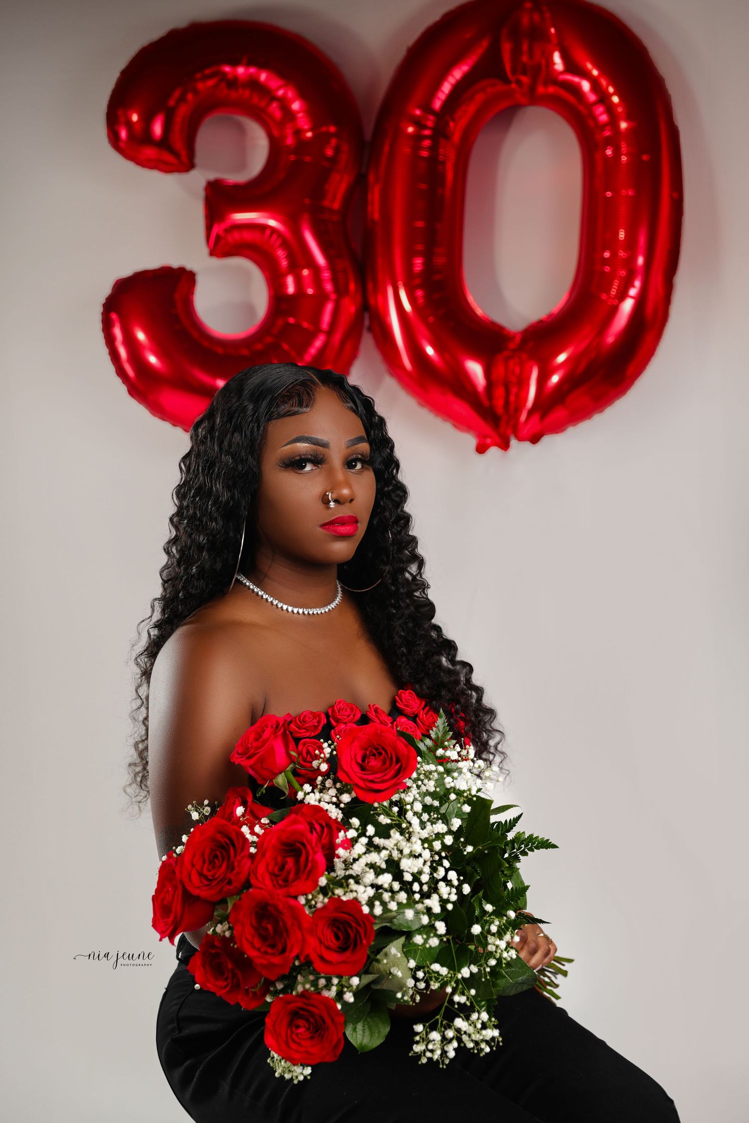 Elegant birthday photoshoot with red balloon numbers and roses against white background.
