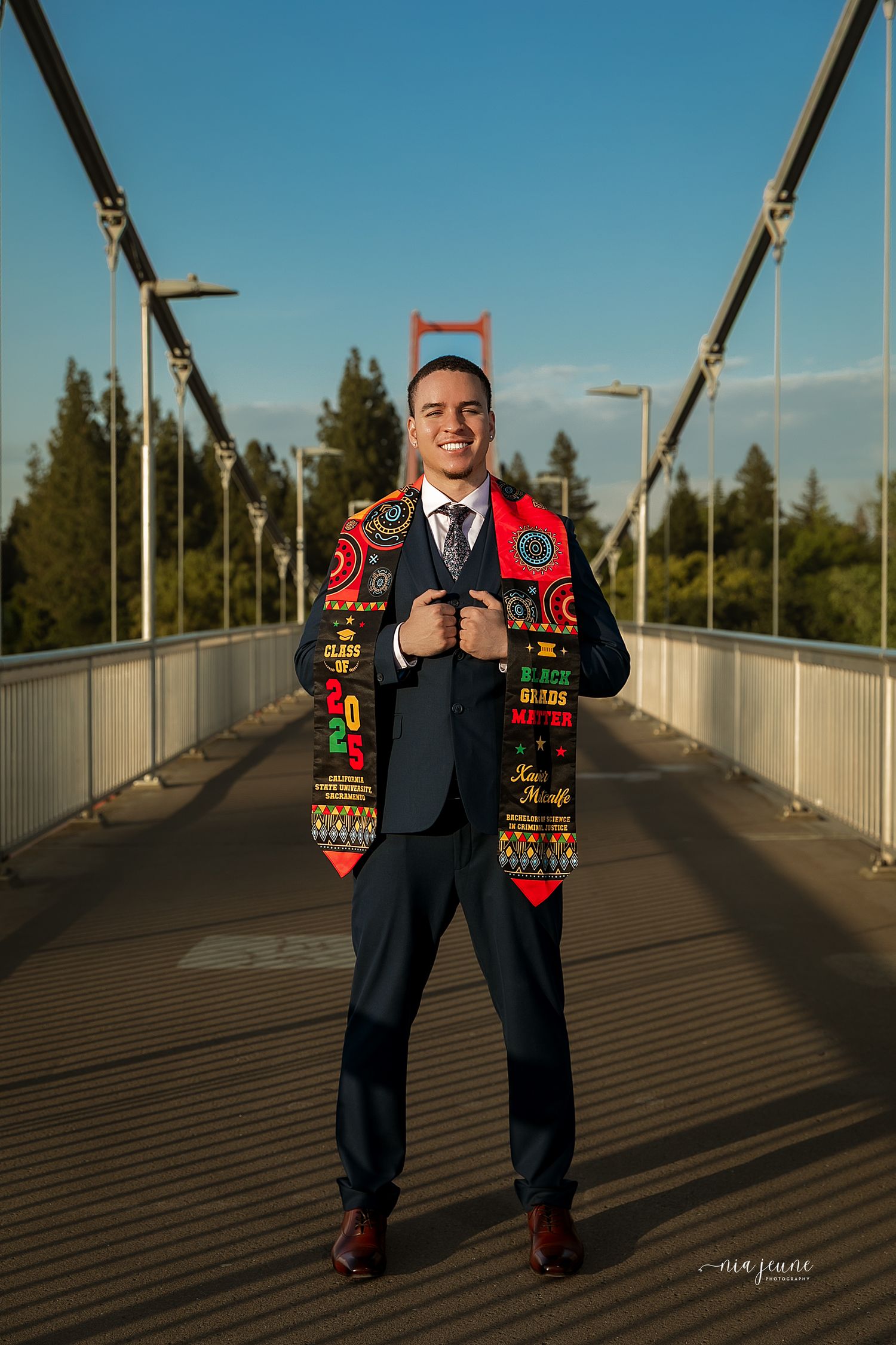 A portrait of someone in a suit with a colorful patterned vest standing on a bridge during golden hour.
