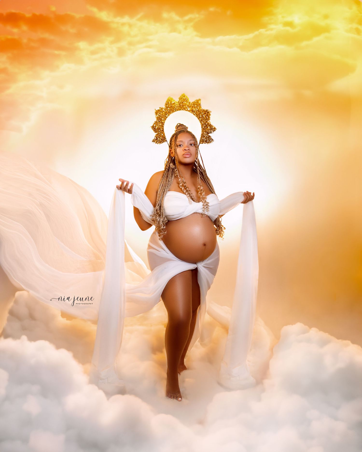 Dreamy maternity photoshoot with flowing fabric against golden sunset clouds.