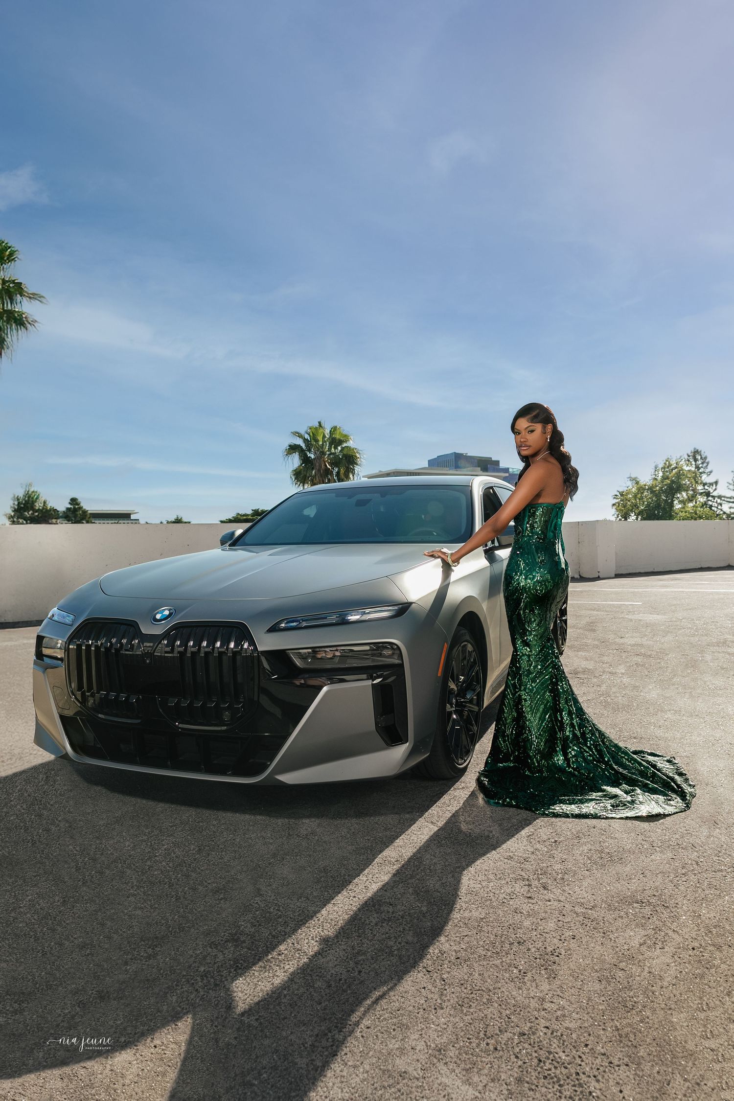 A stunning emerald green mermaid dress paired with a sleek BMW vehicle on a sunny rooftop.