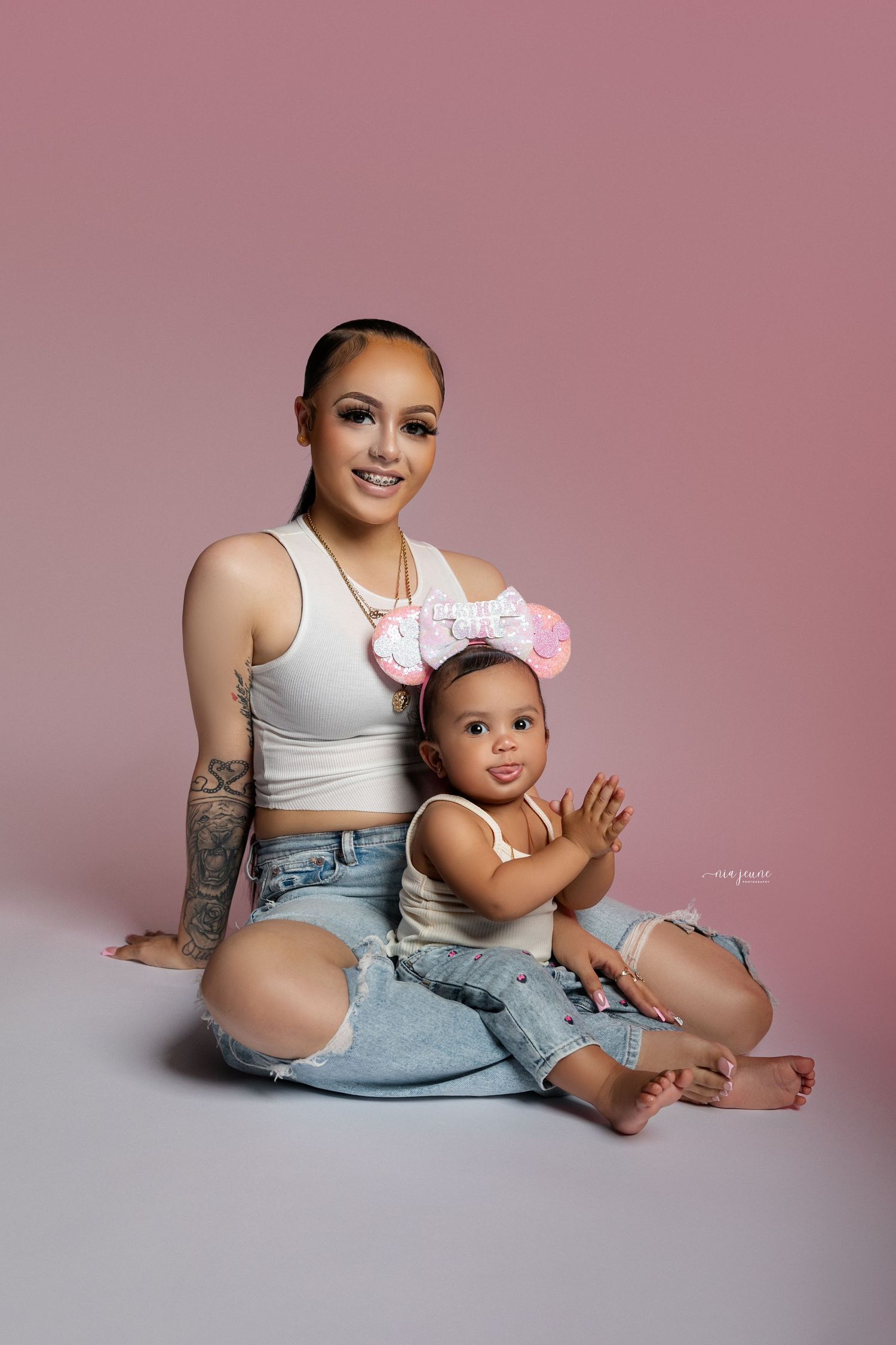 Mother and baby in matching denim and white tops pose during studio photoshoot.