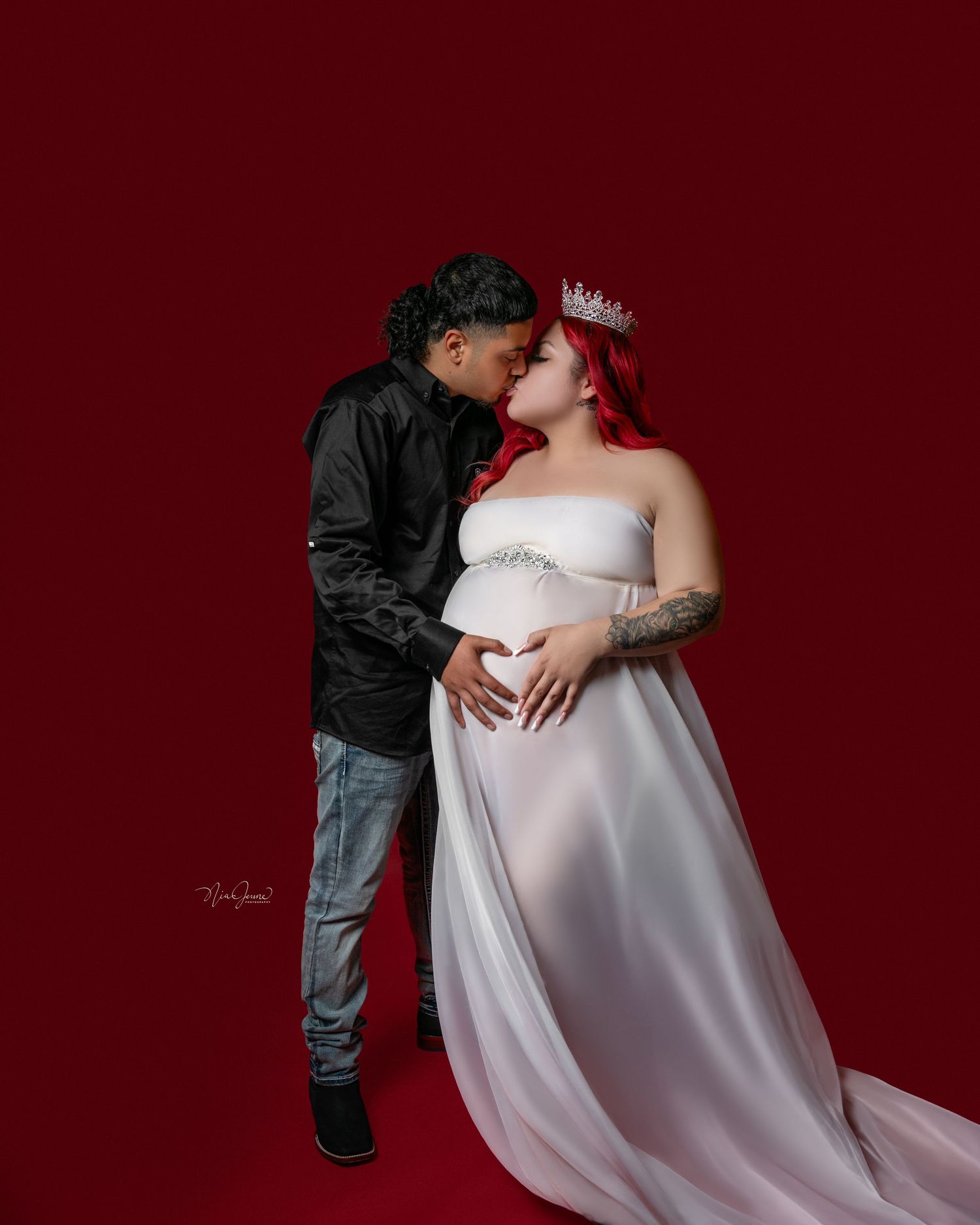 Artistic maternity photoshoot with couple against dramatic red background.
