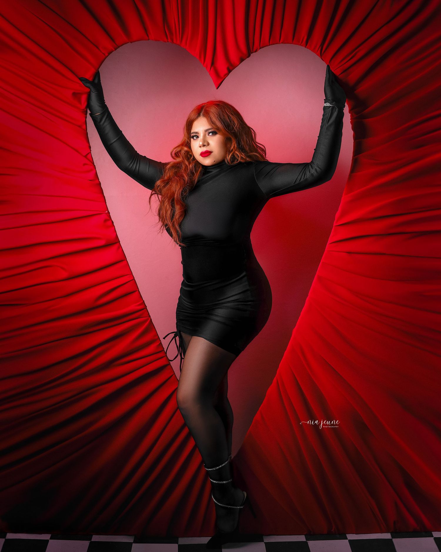 Dramatic portrait against red heart backdrop with radiating lines and black outfit.