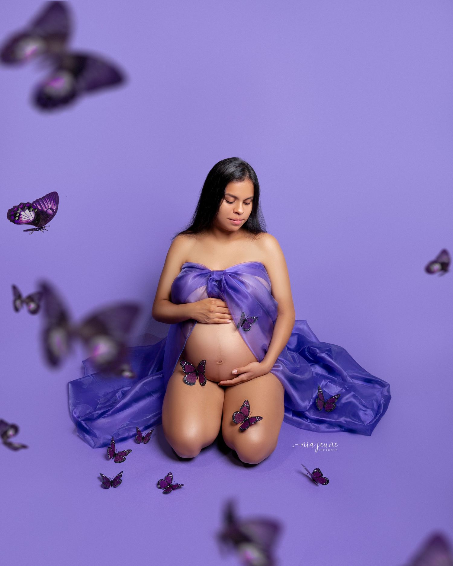Maternity photoshoot with purple fabric and butterfly decorations on a purple background.