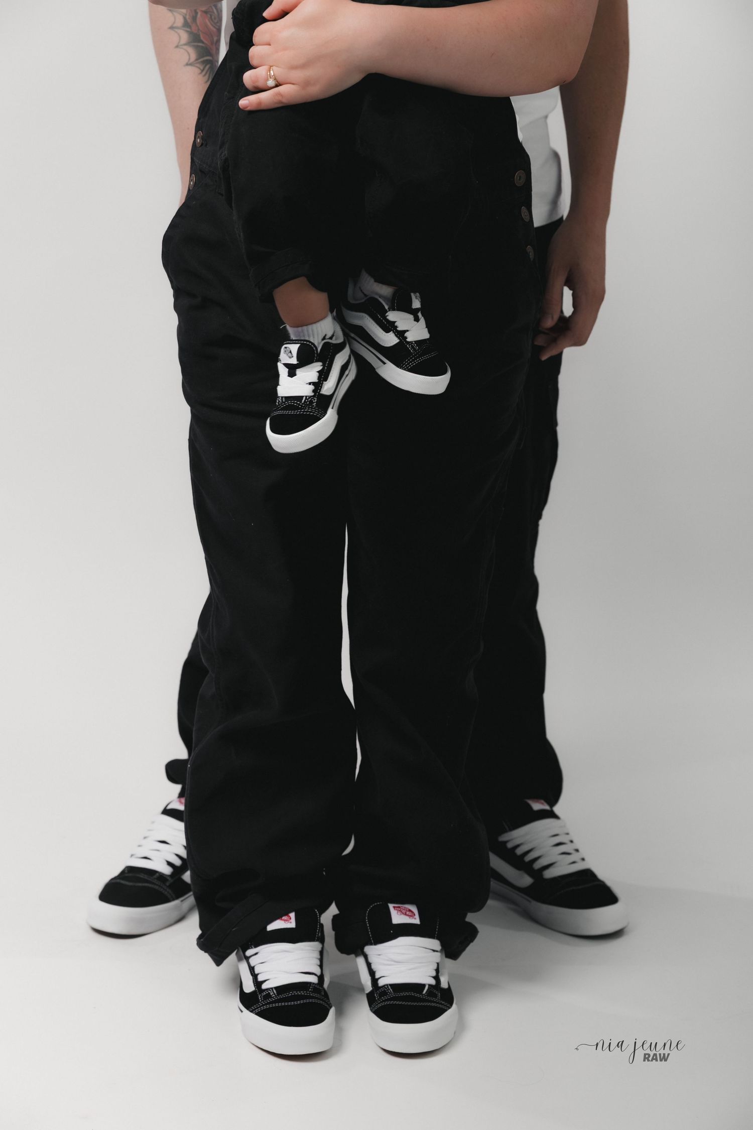 A creative pregnancy announcement showing matching black and white sneakers against dark pants.