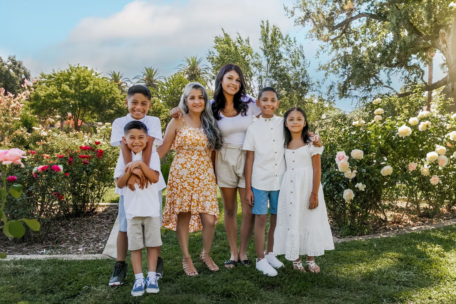 Group portrait of family members posing together in a garden with white flowers and greenery.