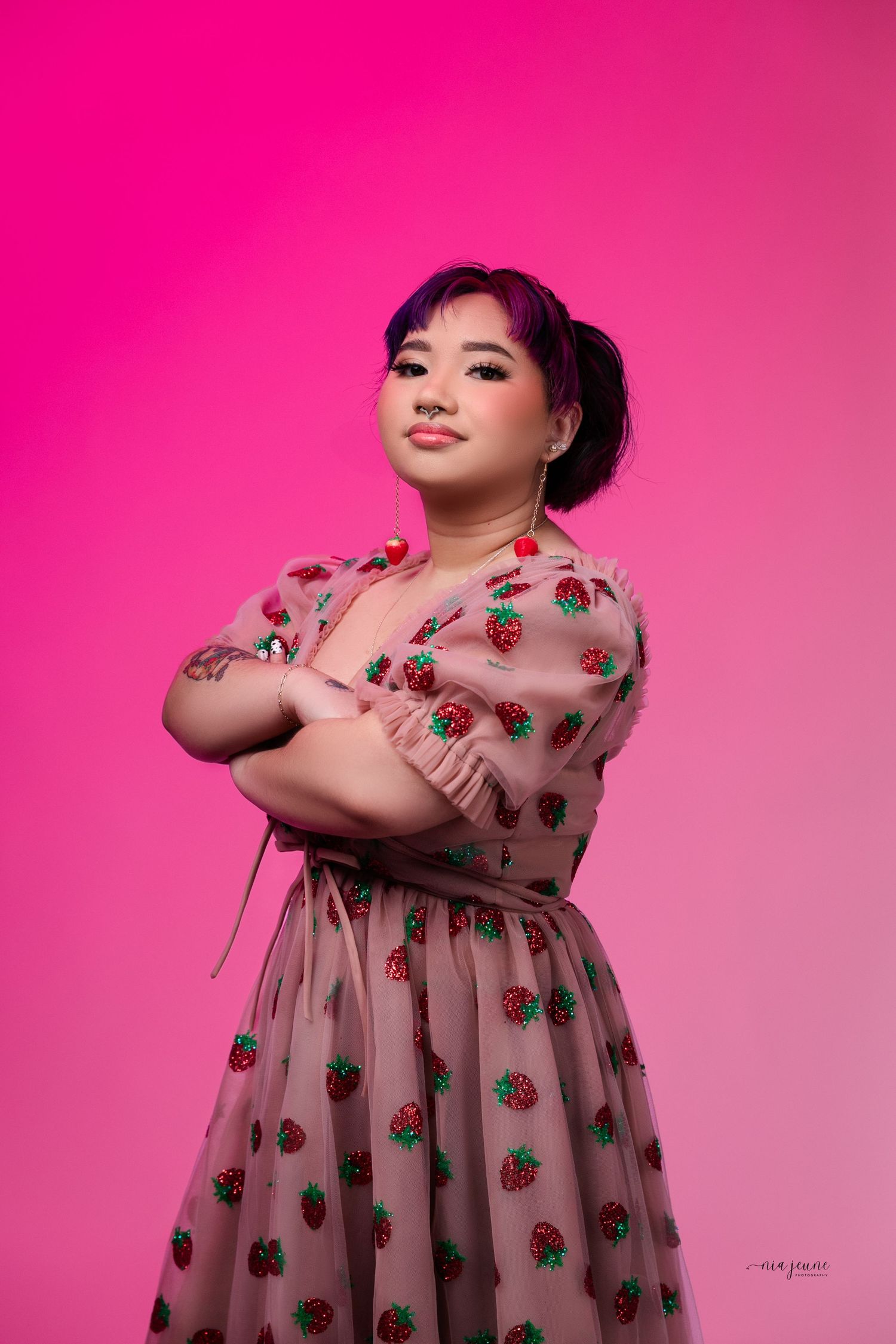 Fashion portrait with strawberry print dress against vibrant pink background.
