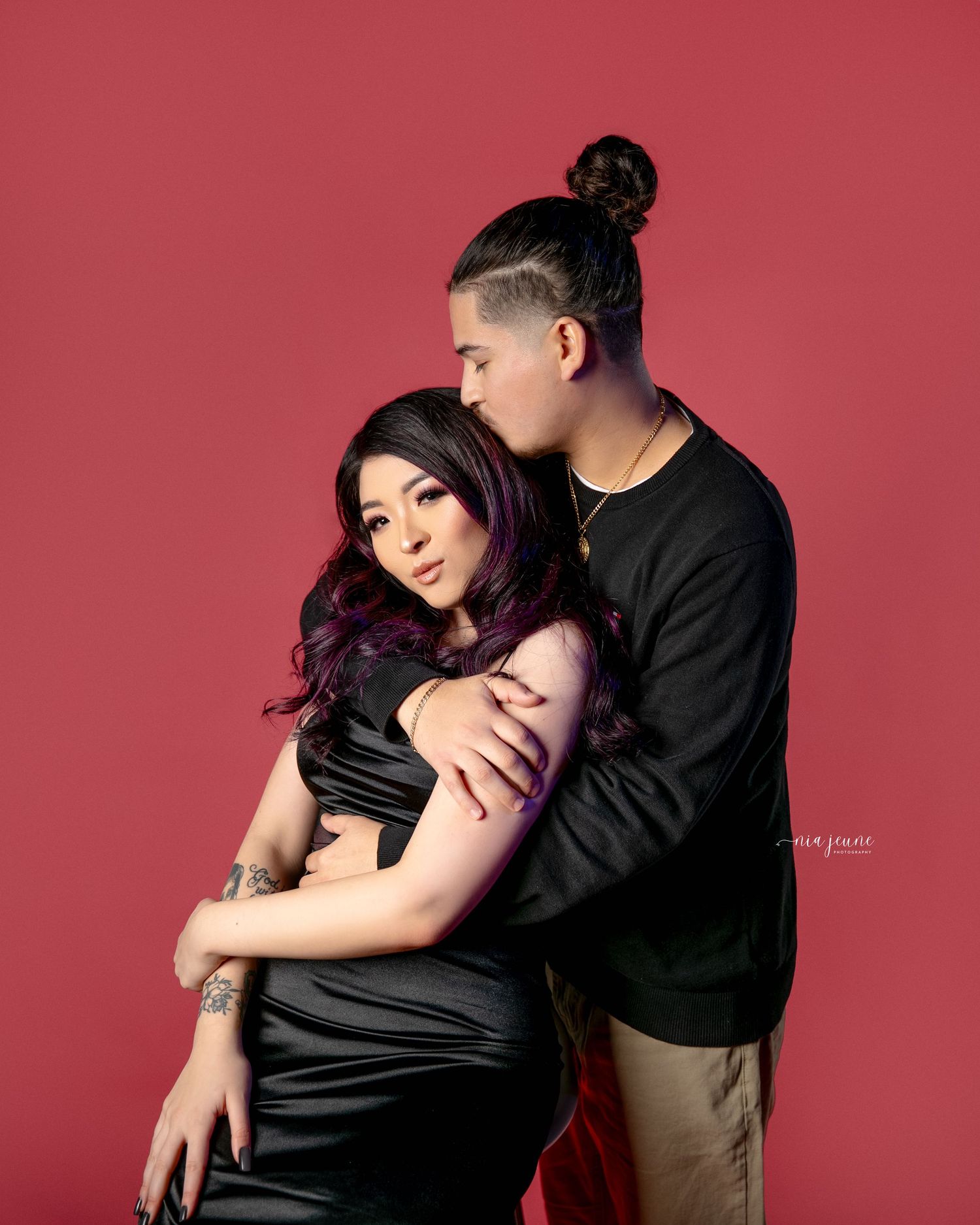 Romantic couple portrait against red background showing intimate embrace.