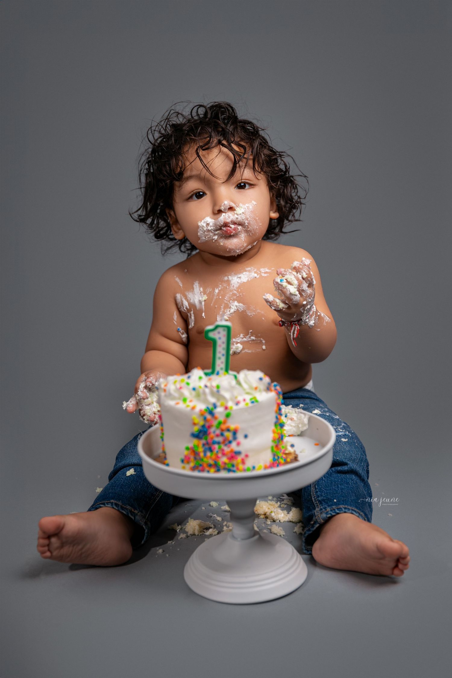 Baby's first birthday cake smash photoshoot with colorful frosting and sprinkles.