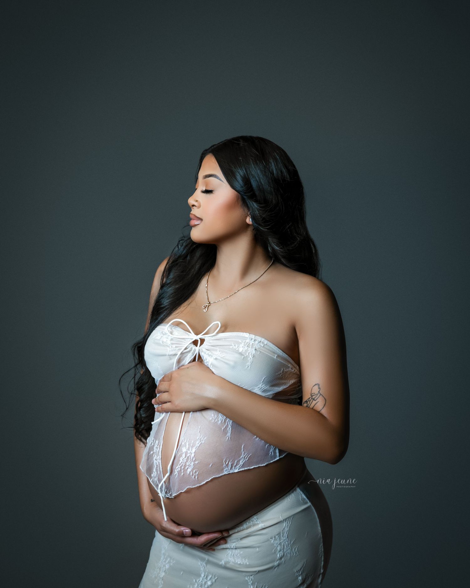 Elegant maternity portrait in white sheer fabric against dark backdrop.