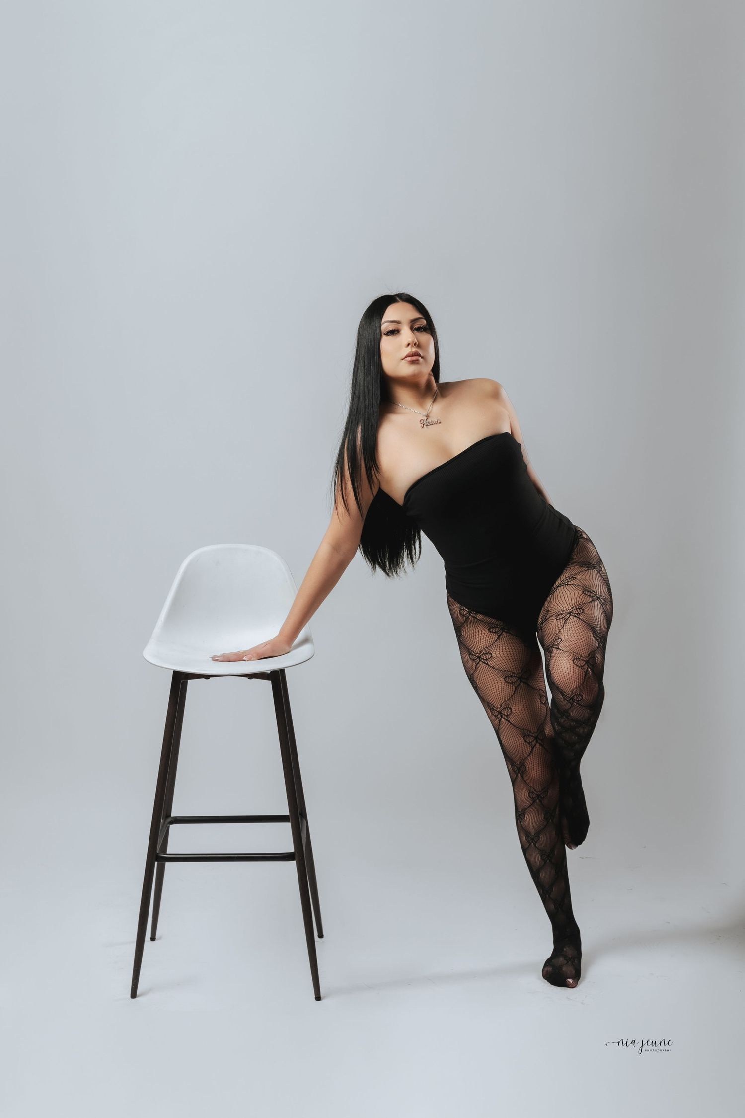 Artistic fashion photography series featuring a model in black lace posing with a white modern bar stool against gray backdrop.