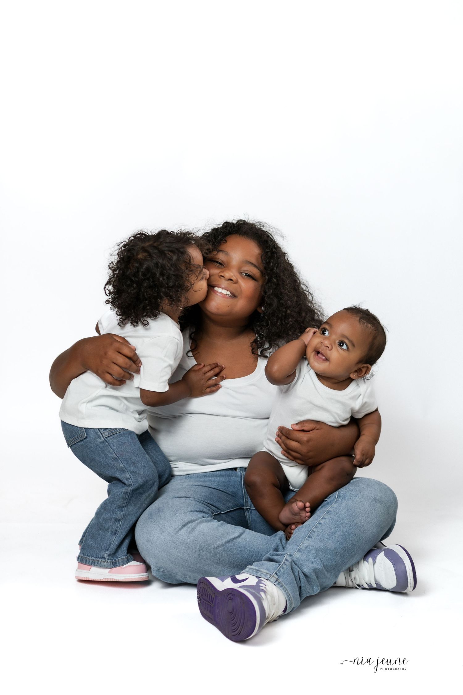 A joyful family moment captured against a white backdrop as they sit together on the floor wearing casual attire.