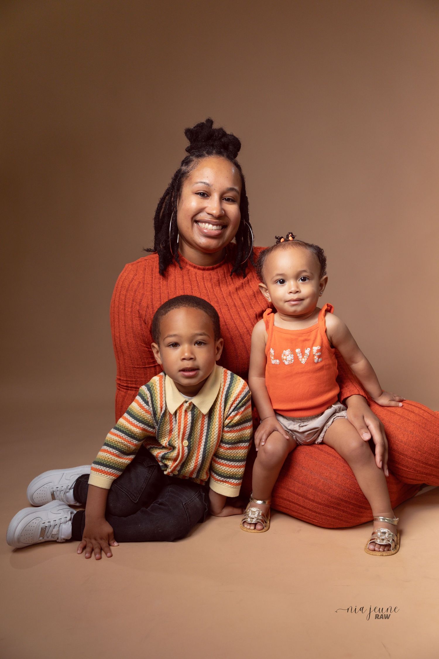 A family portrait featuring bright orange themed clothing against a warm brown backdrop.