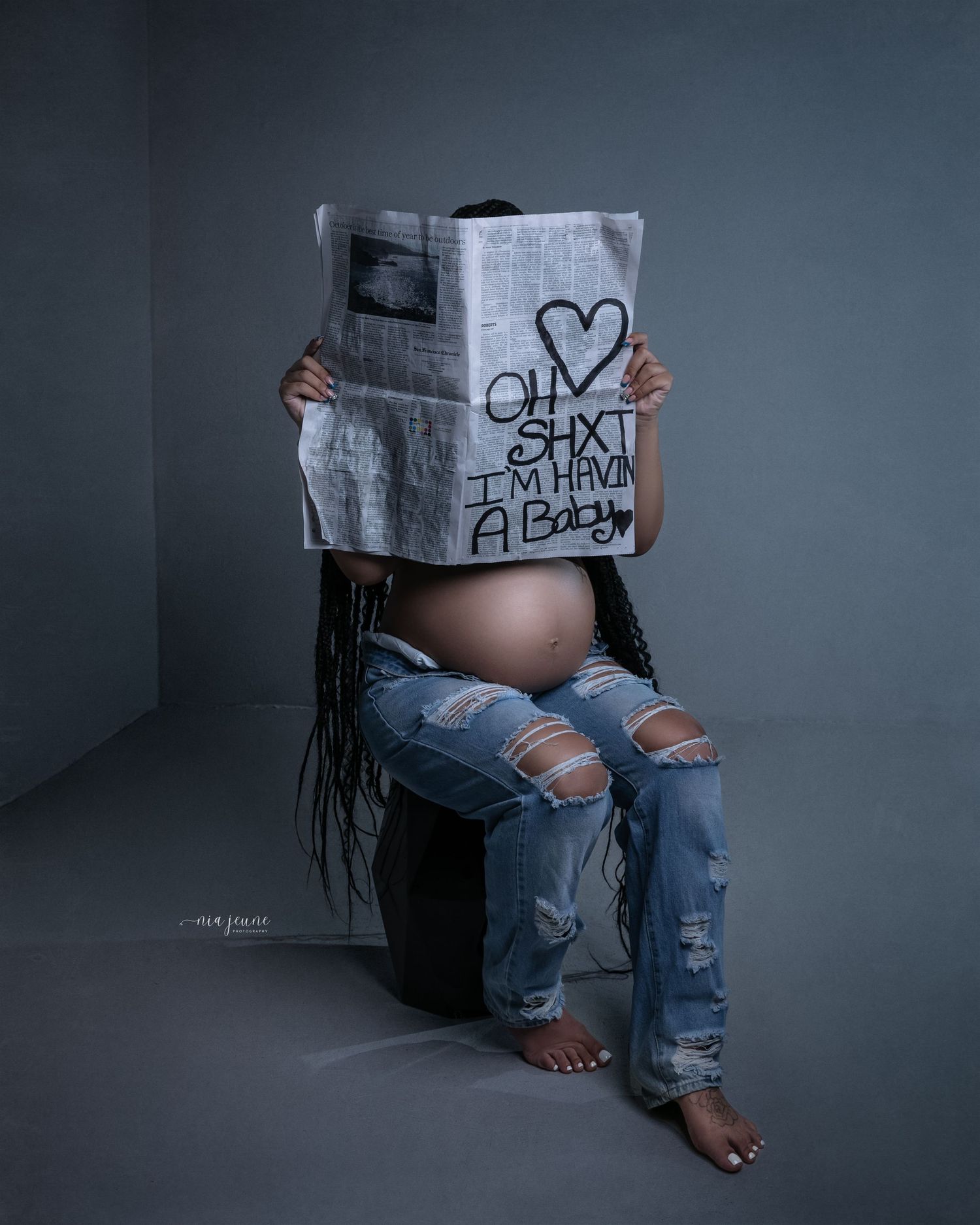 Creative maternity photos showing baby announcement messages on paper against dark background.