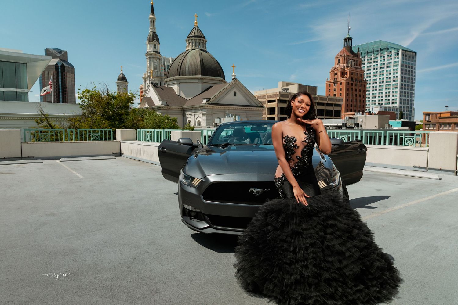 Dramatic portrait with flowing black dress and Ford Mustang on urban rooftop.