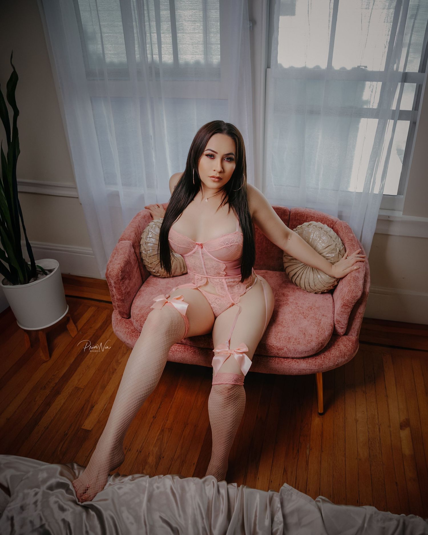 Boudoir photography in a bright room with pink velvet chair and sheer curtains.