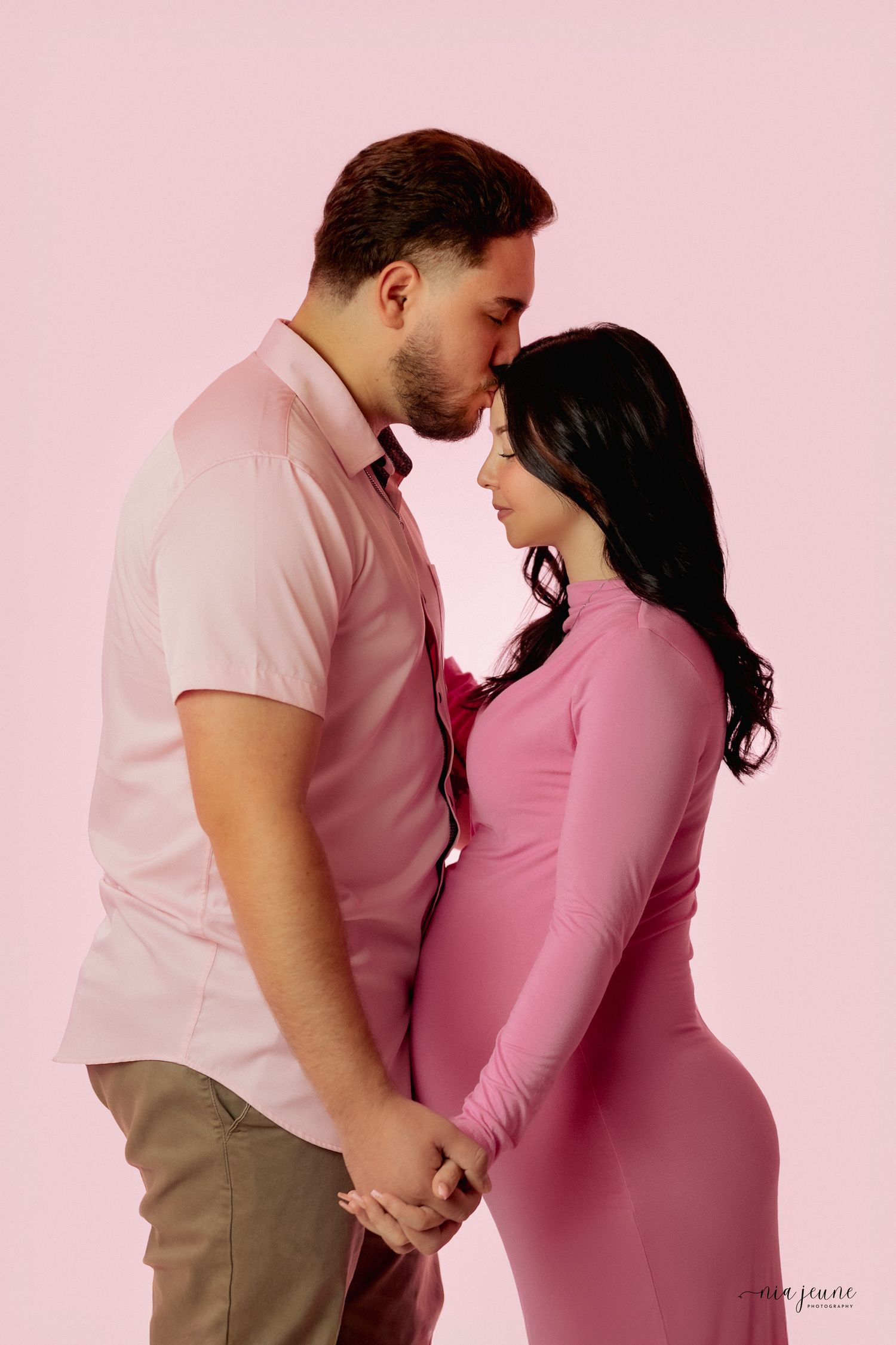 Romantic maternity photo series showing couple in matching pink and beige outfits against pink backdrop.