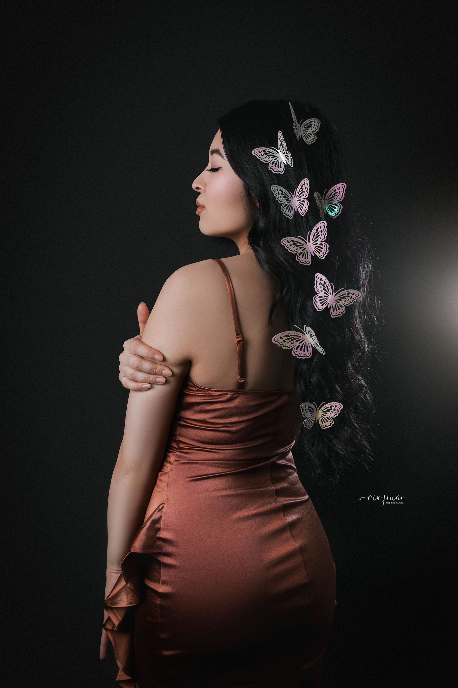 Artistic portrait with delicate butterfly decorations adorning dark hair against a moody background.