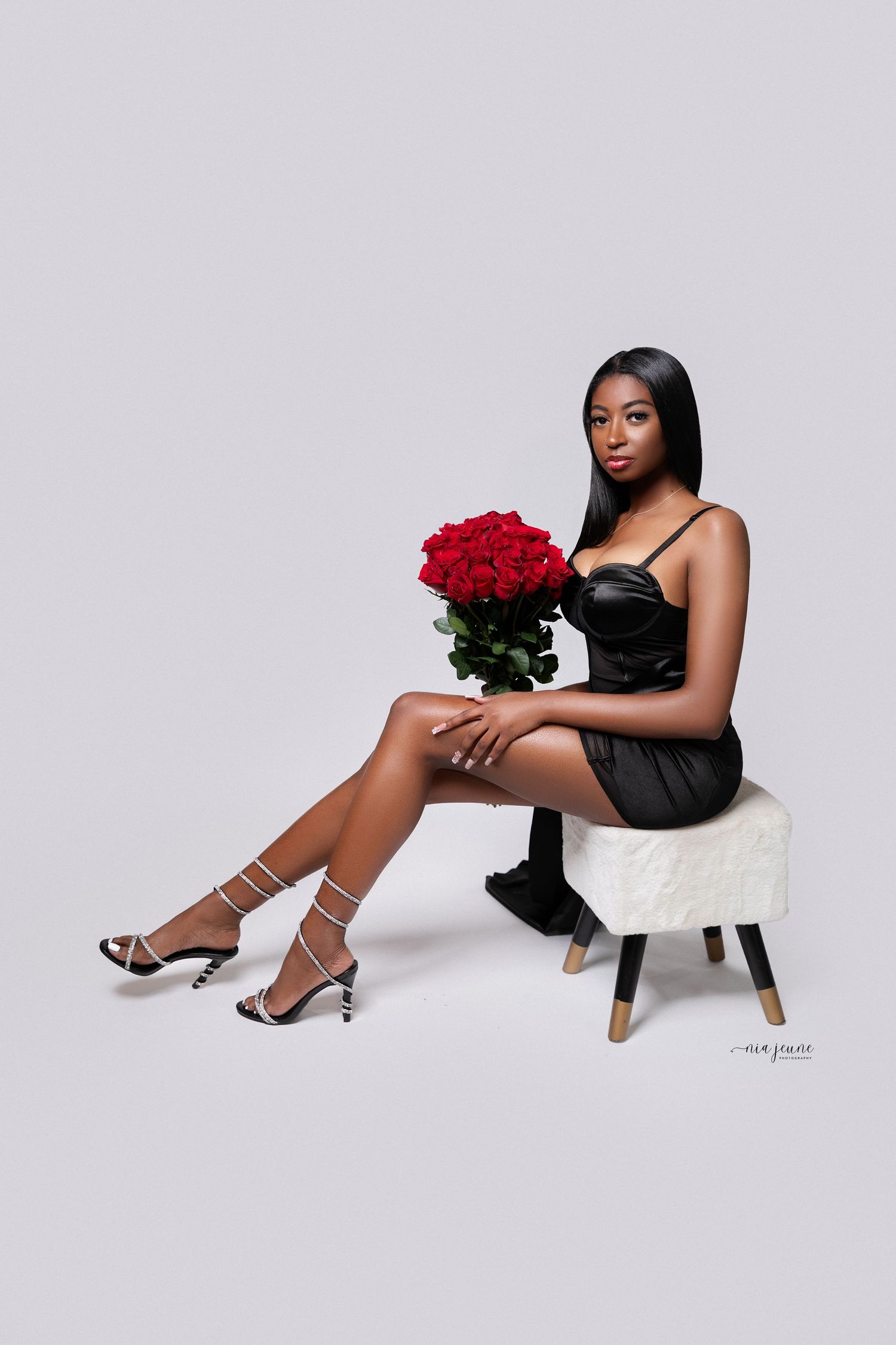 Elegant portrait with red roses on white stool against minimal gray background.