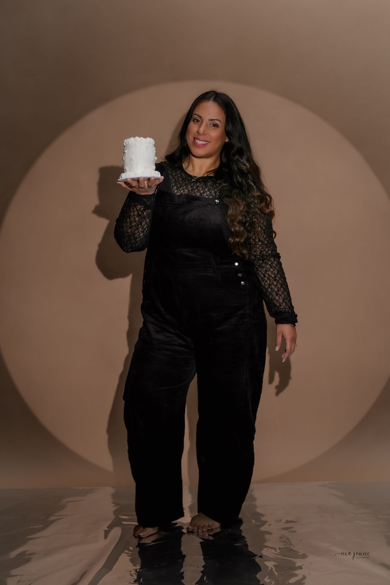Woman in elegant black lace dress poses confidently against neutral backdrop in professional photoshoot series.
