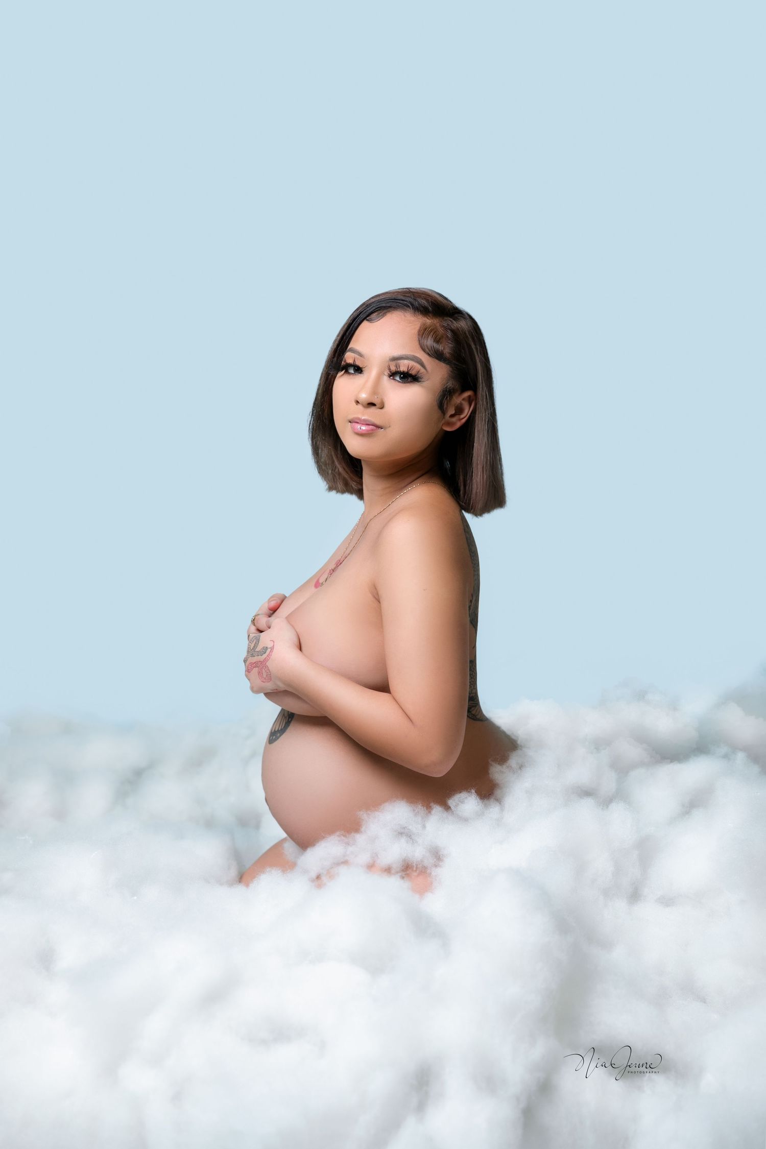 Ethereal maternity portrait with clouds against light blue background.