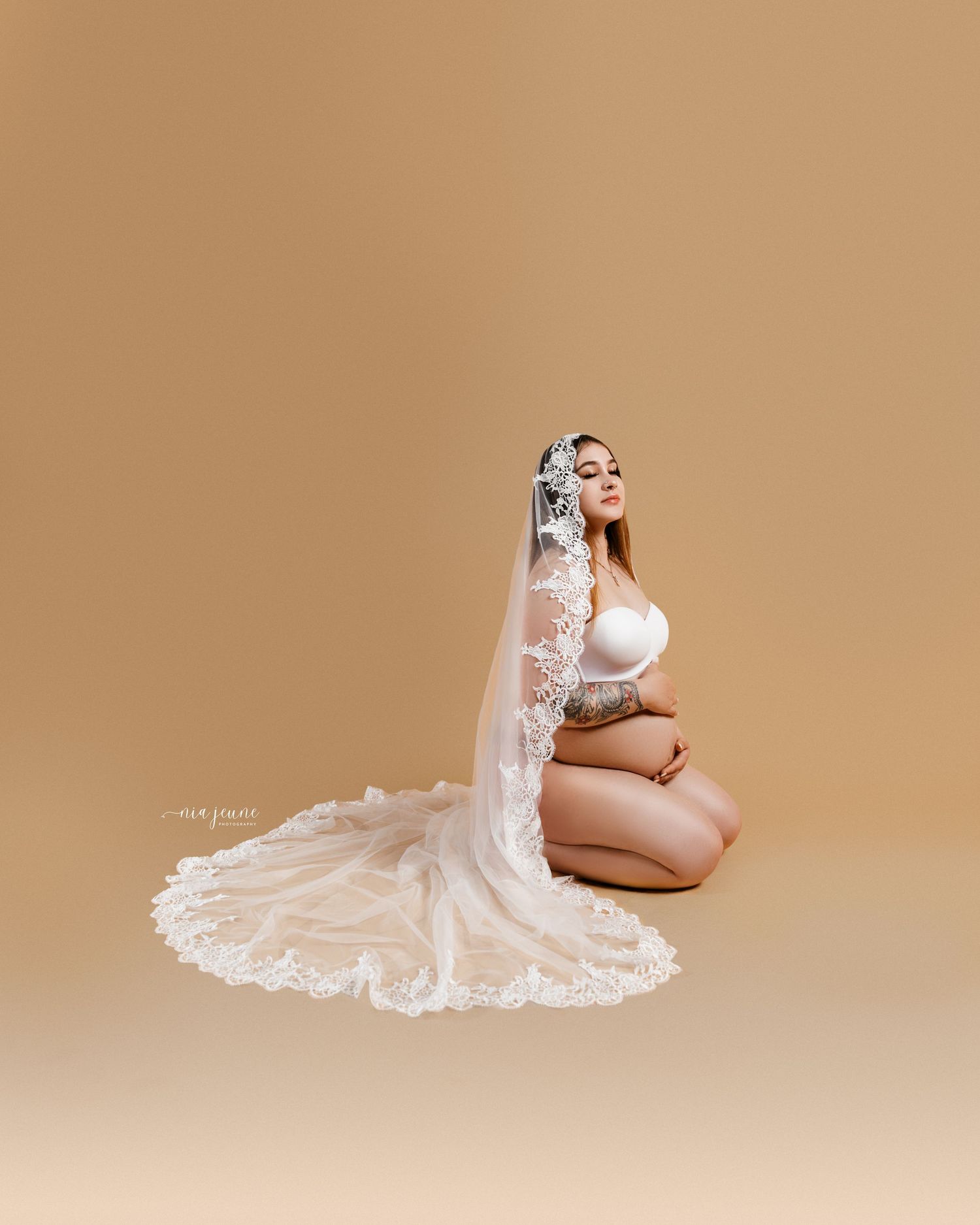 Artistic maternity photos with elegant white lace veil against warm beige background.