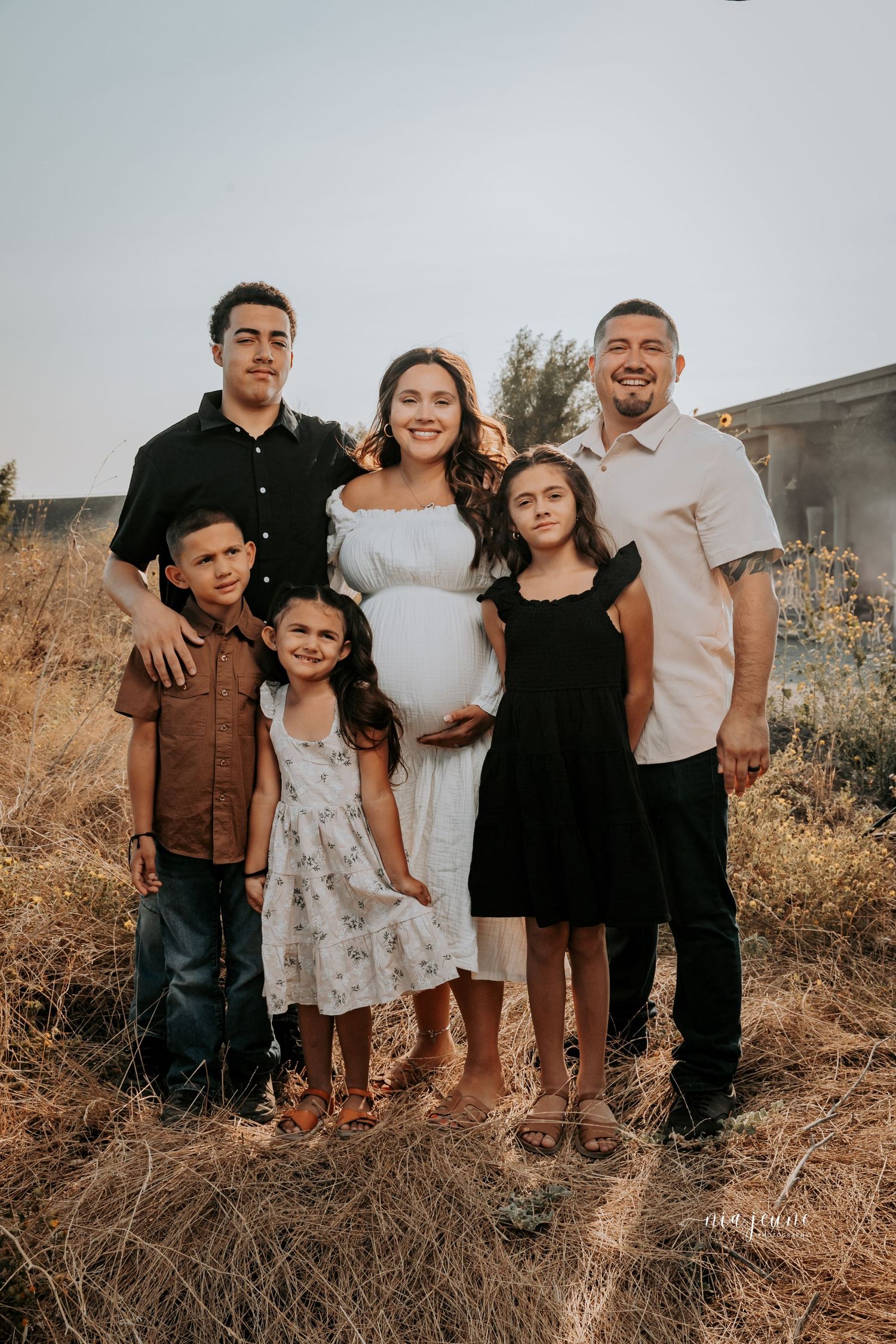 Family group portrait with coordinated outfits standing in golden field at sunset.