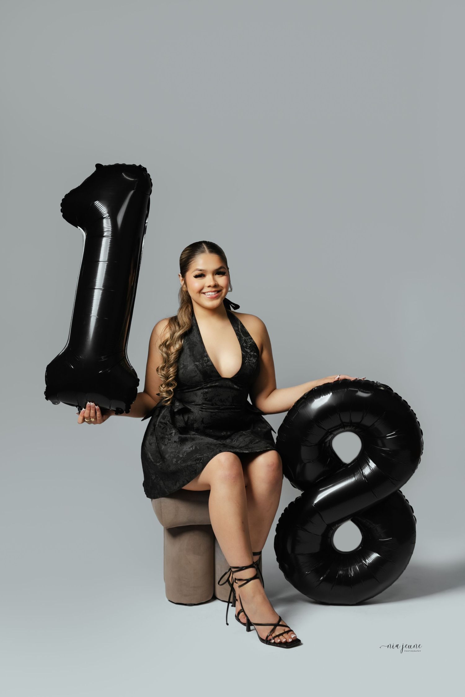 Studio photo series showing someone posing with large black inflatable number 8 balloons against a gray background.