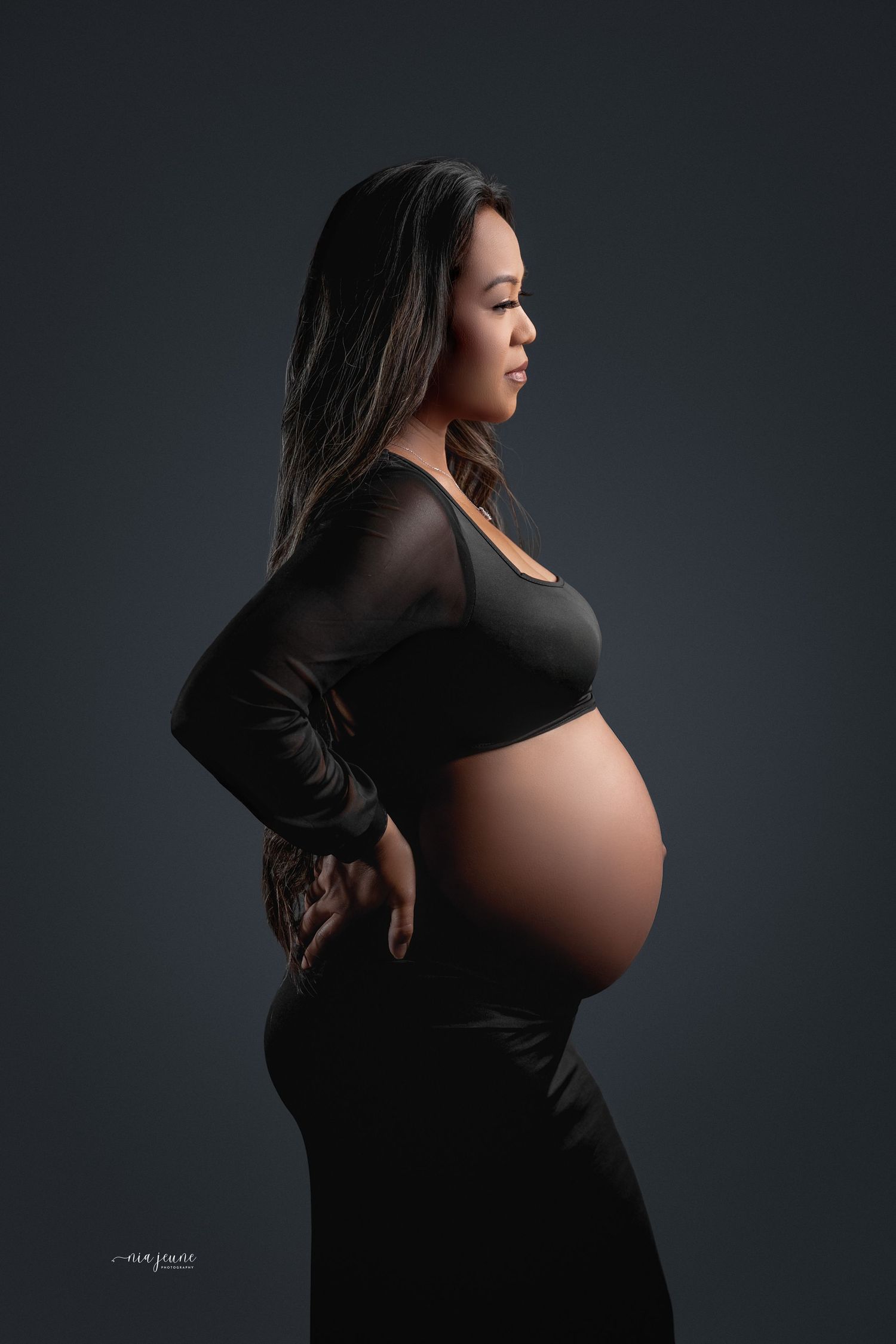 Dramatic maternity silhouette portrait against dark background.