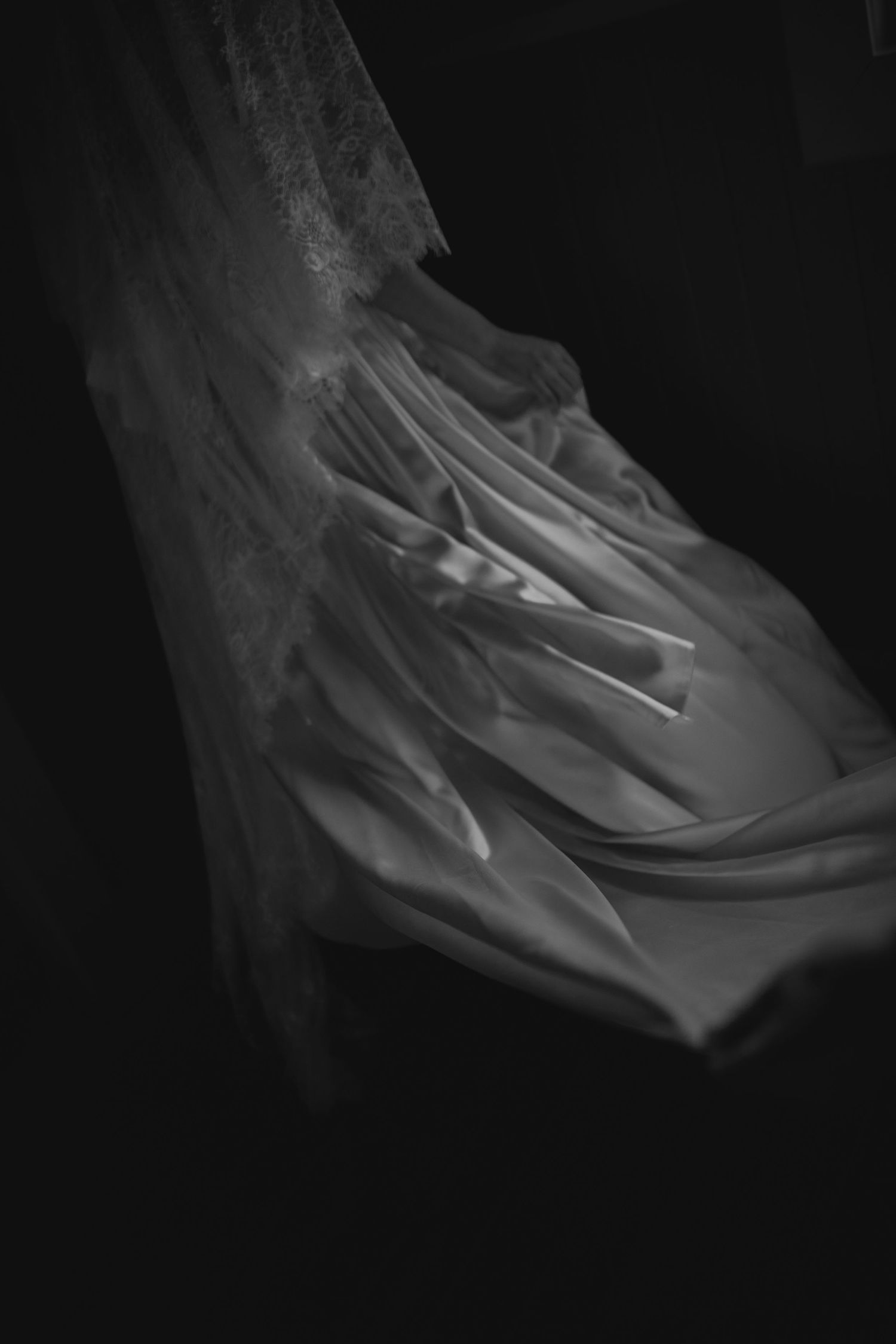 Black and white photo of flowing sheer bridal veil fabric draped elegantly against a dark background.