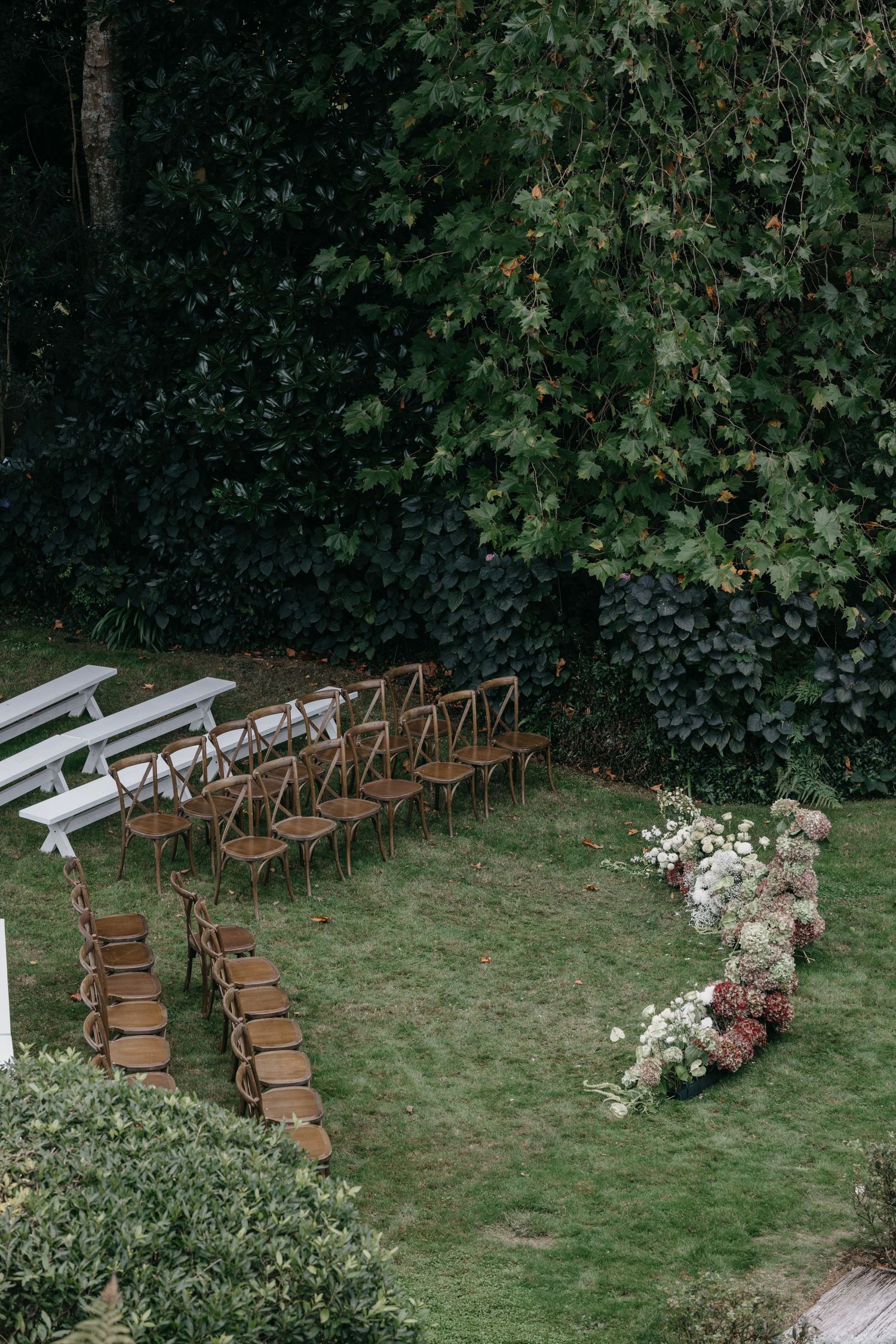 An aerial view of an elegant outdoor wedding ceremony with wooden chairs and a beautiful floral ground arrangements.