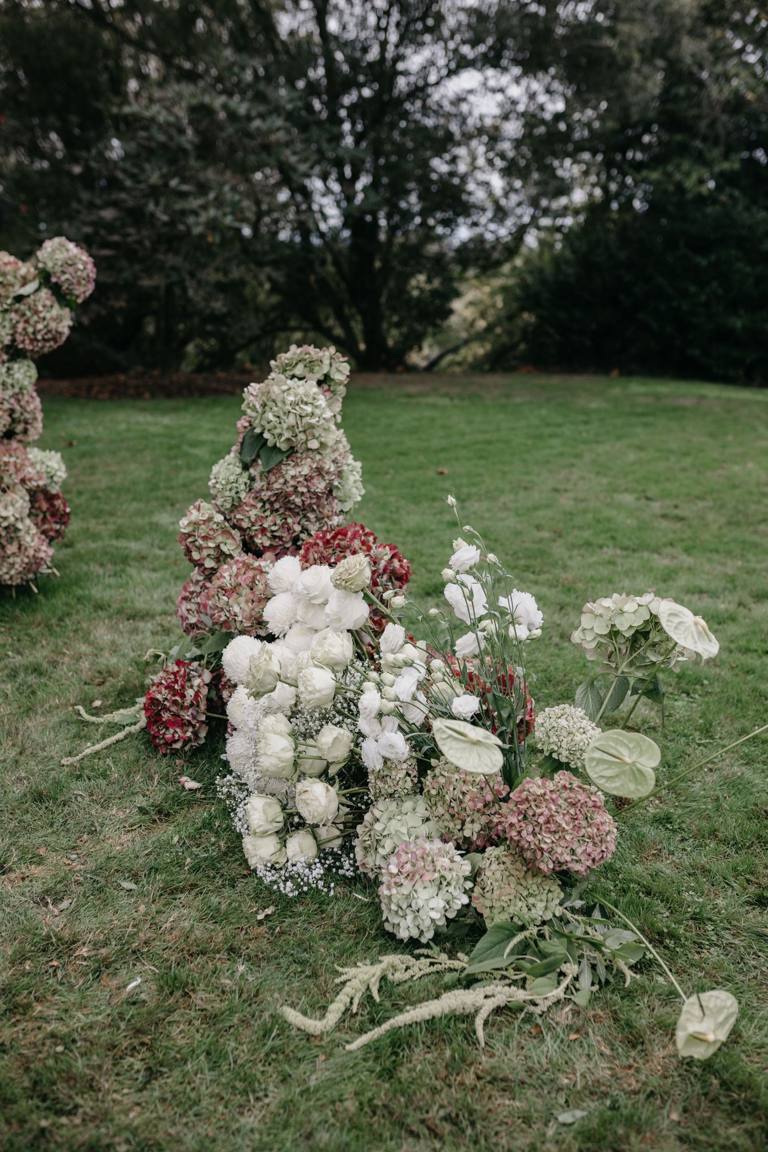 Elegant outdoor floral arrangement with white roses and pink hydrangeas on green grass for a garden wedding ceremony.