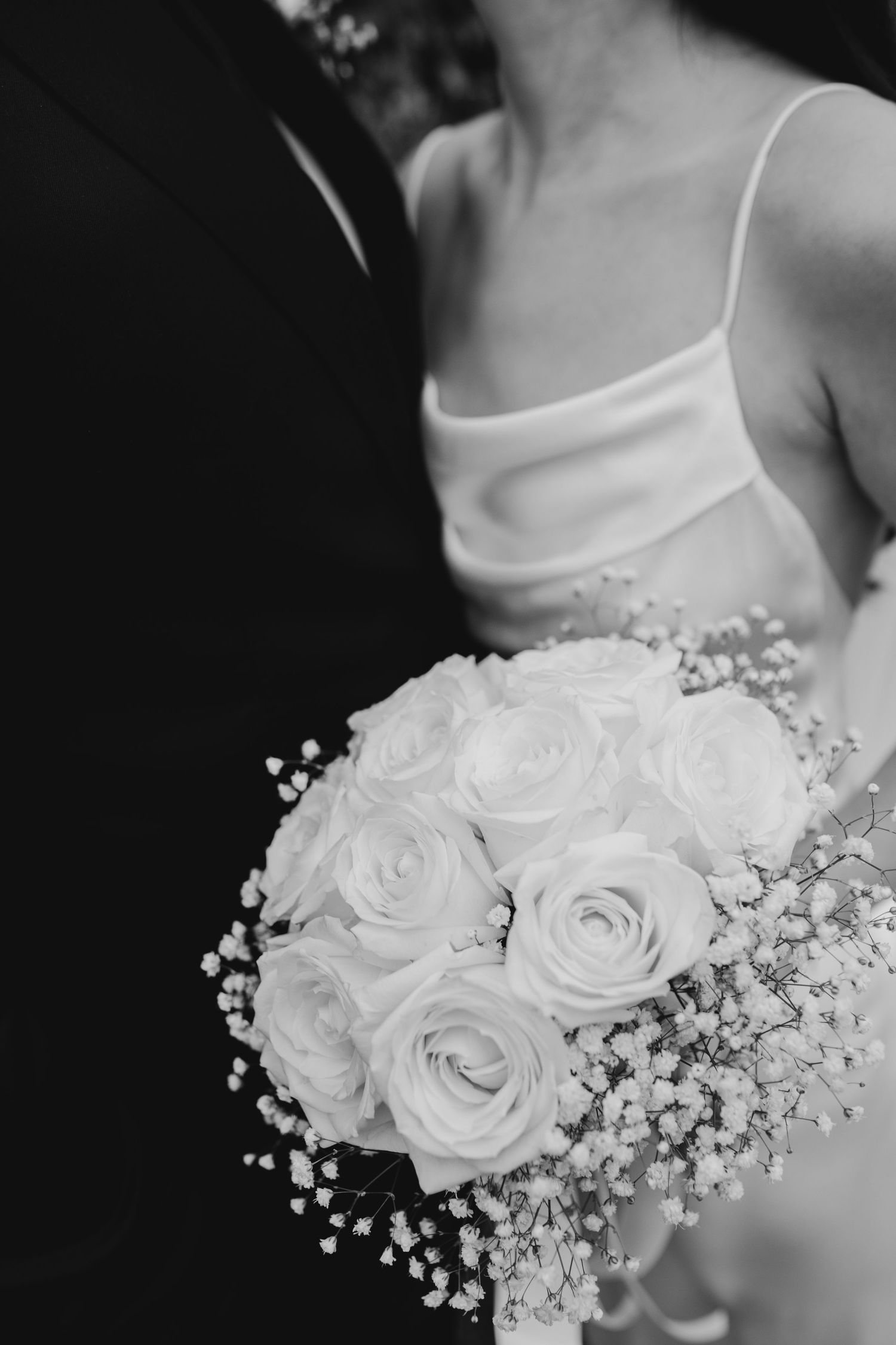 A black and white close-up of a bridal bouquet featuring white roses and delicate baby's breath flowers.