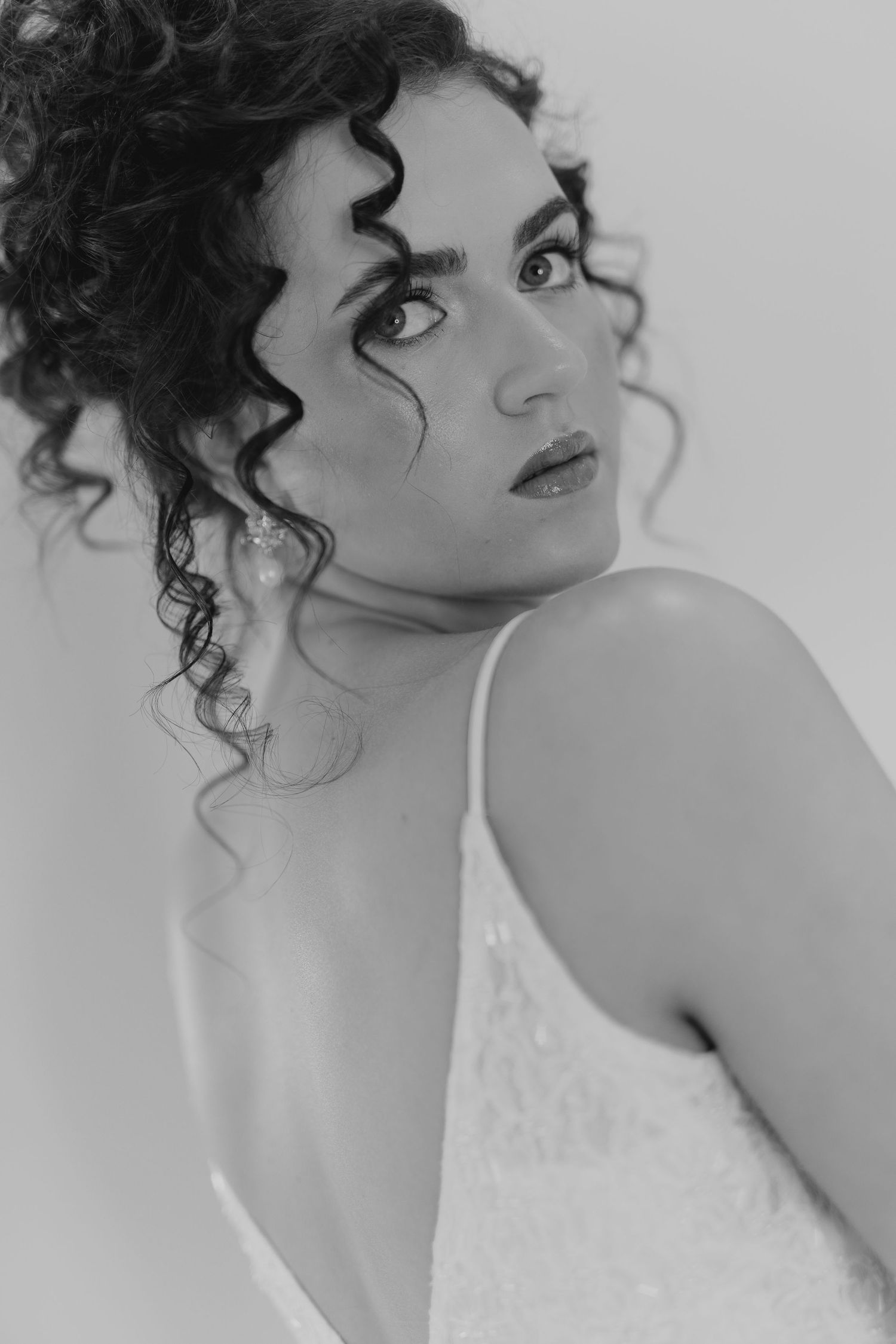 Black and white portrait of a bride with curly hair wearing a lace gown and pearl earrings.
