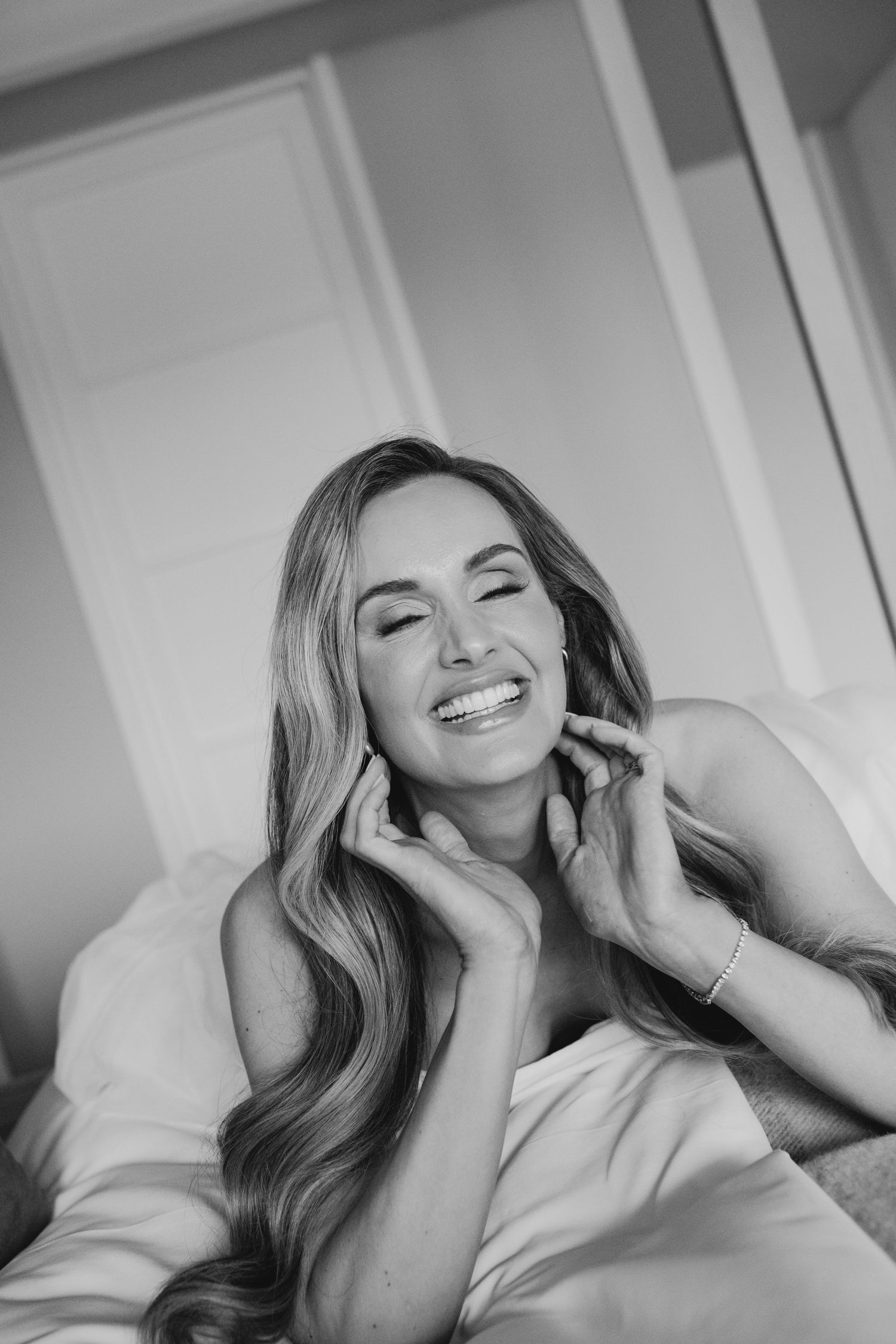 Black and white portrait of a smiling woman with long wavy hair, sitting relaxed with hands near her face.