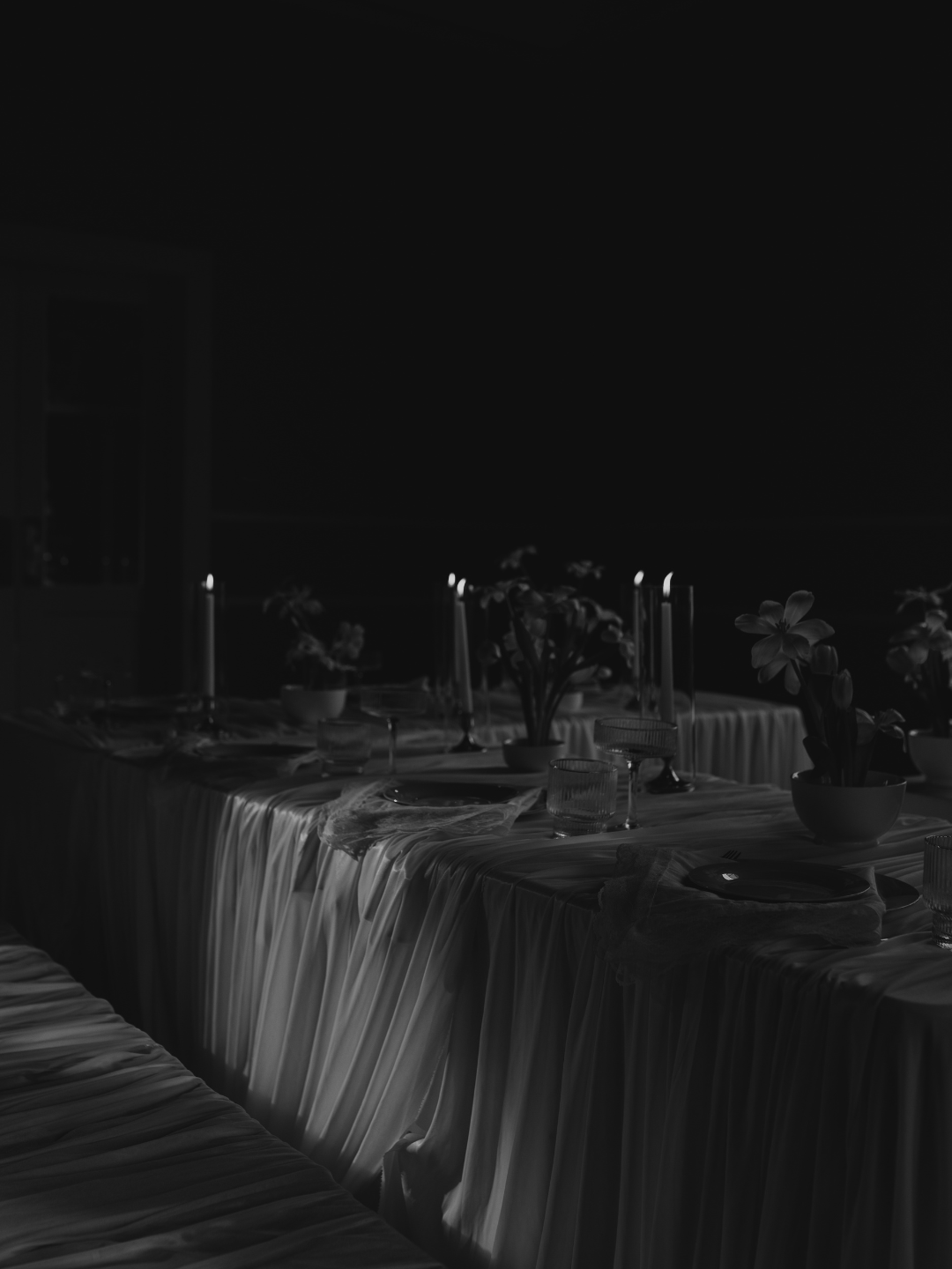 Black and white photo of an elegant candlelit dinner table set with candles, flowers, and fine dinnerware.